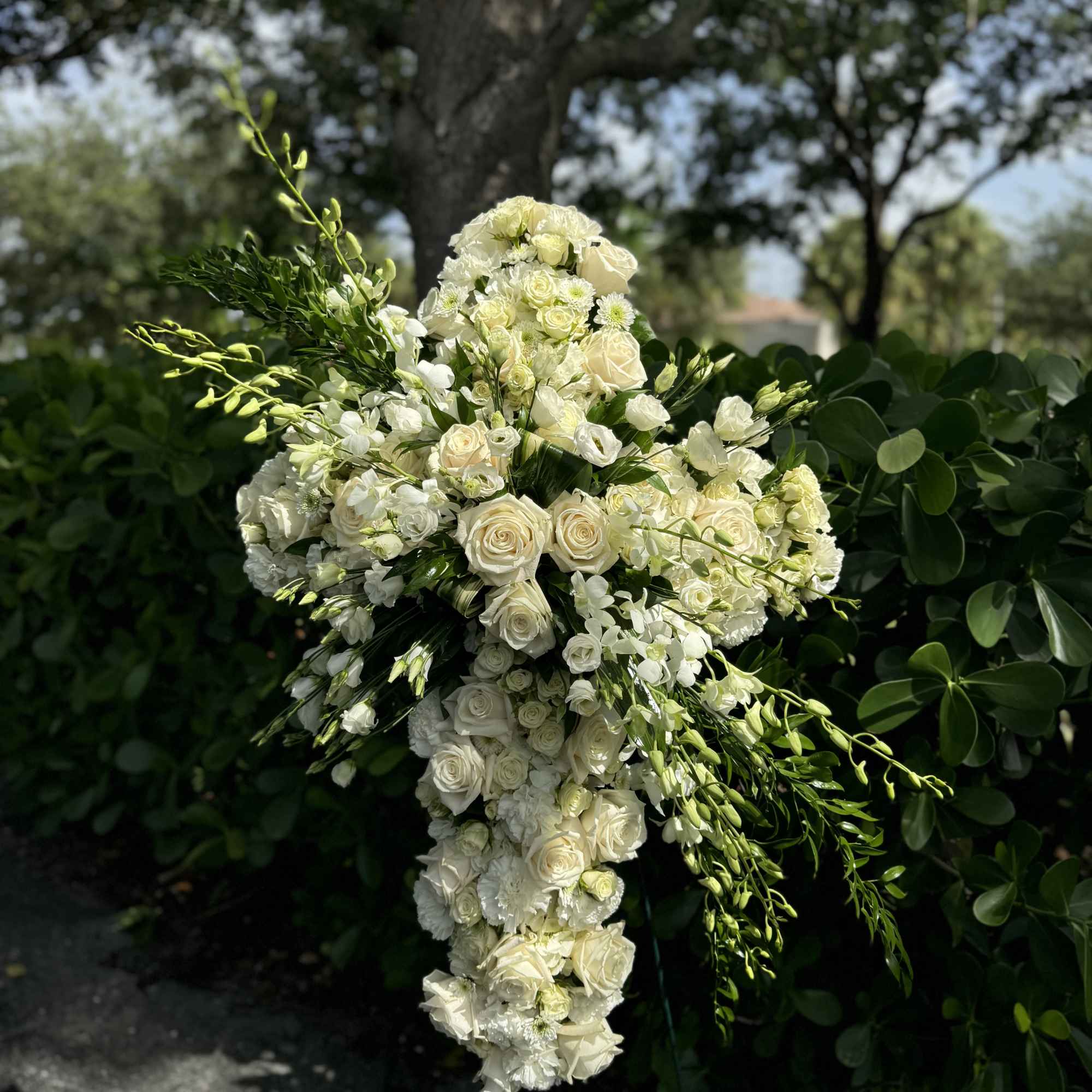 White floral cross-shaped arrangement with roses and orchids