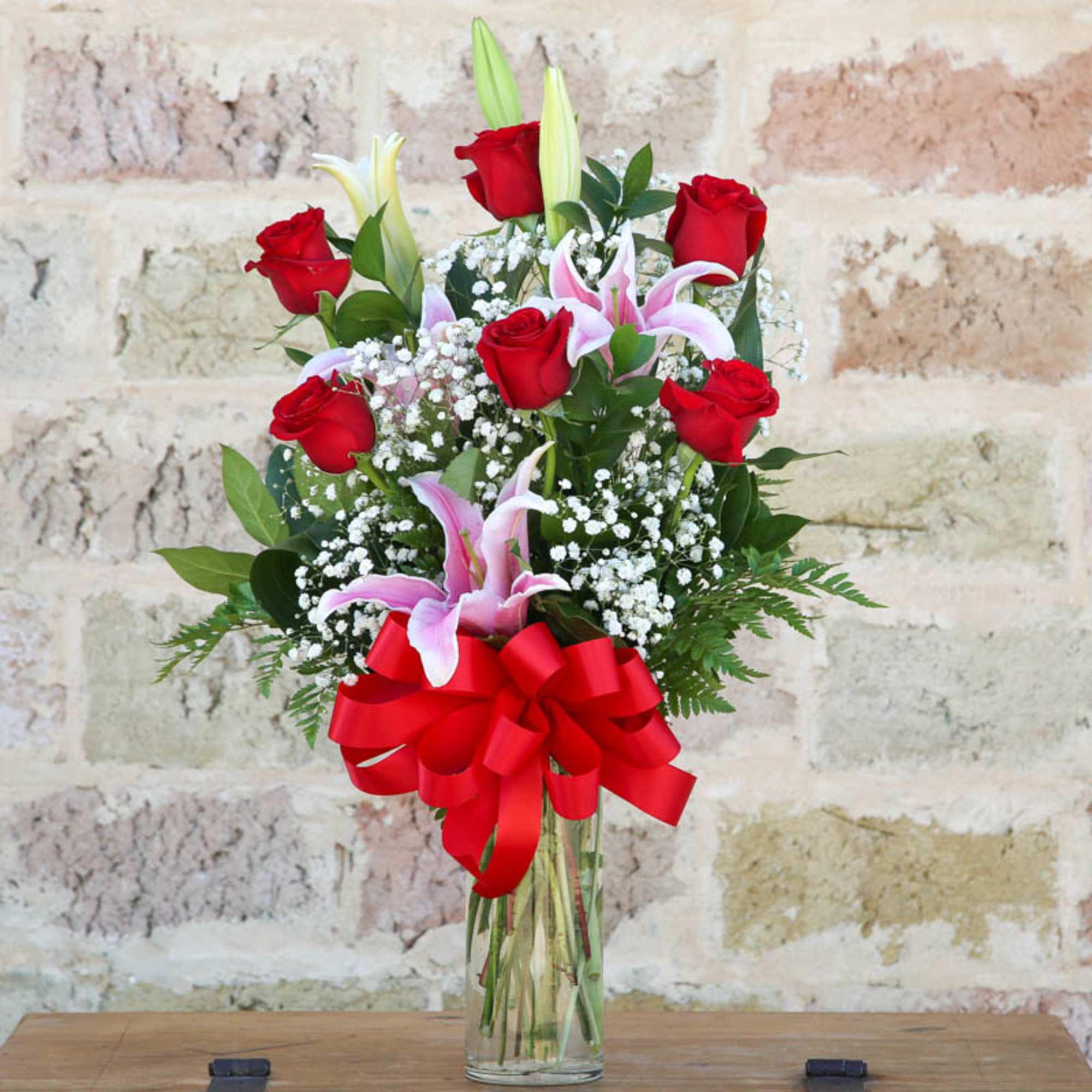 Bouquet of red roses and pink lilies in a clear glass vase with a red bow