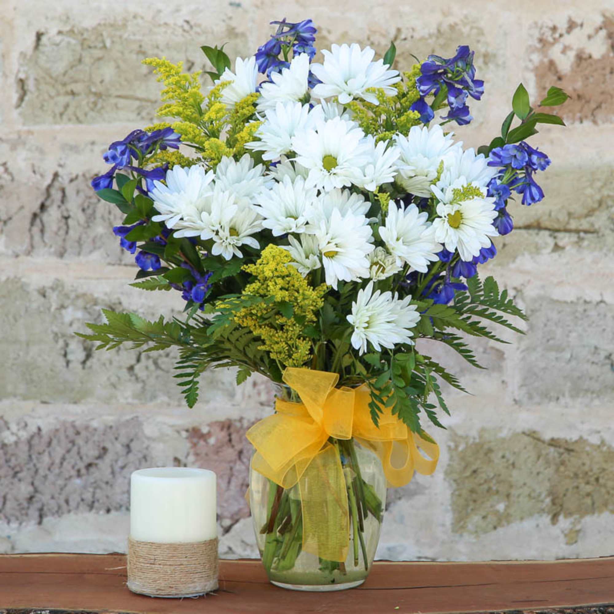 Bouquet of white daisies and blue flowers in a glass vase with a yellow ribbon