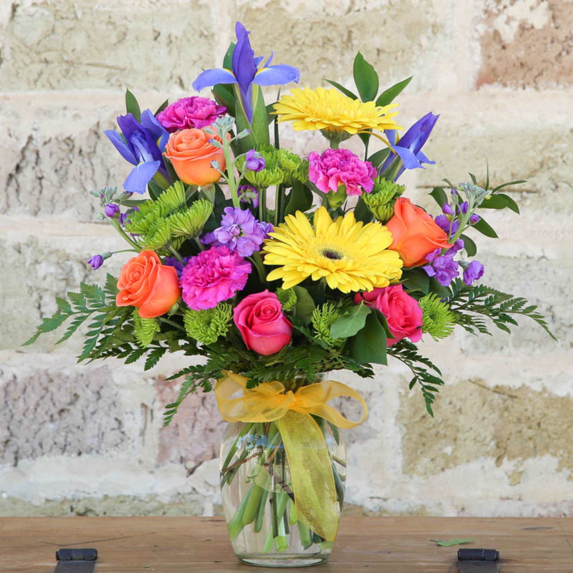 Colorful bouquet of roses, gerbera daisies, and purple flowers in a glass vase