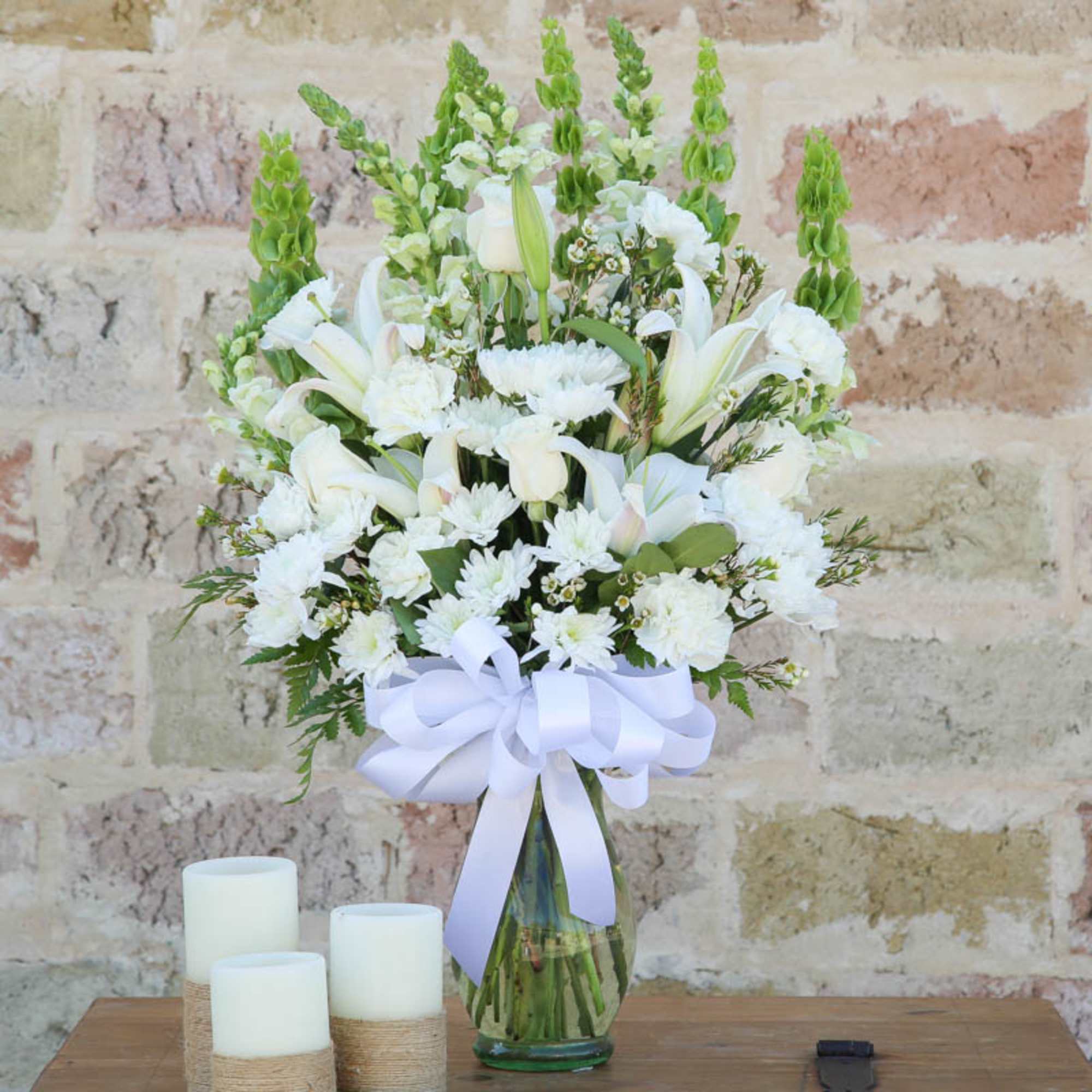 White floral arrangement in a glass vase with a lavender ribbon