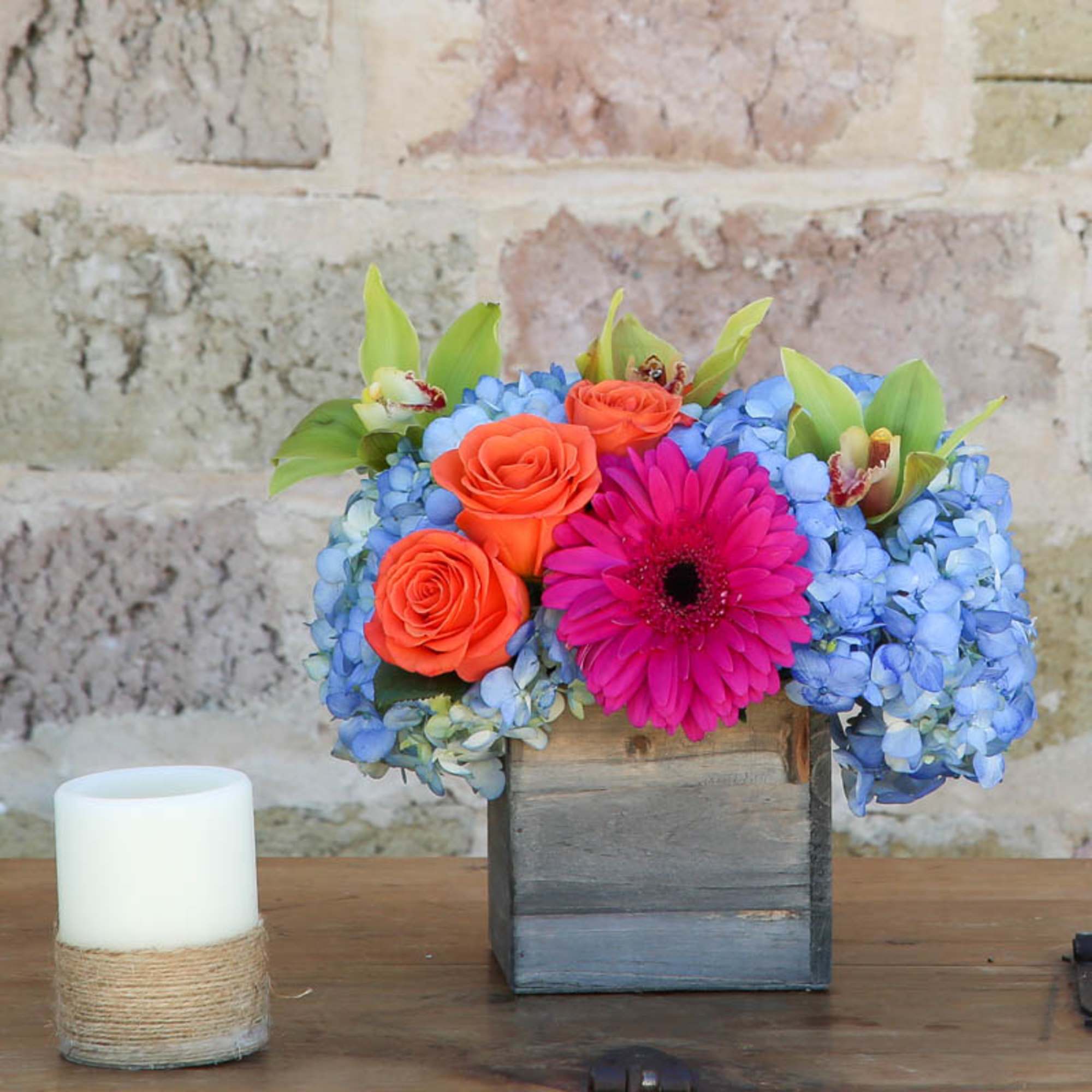 Blue hydrangeas with orange roses and a pink gerbera in a wooden box