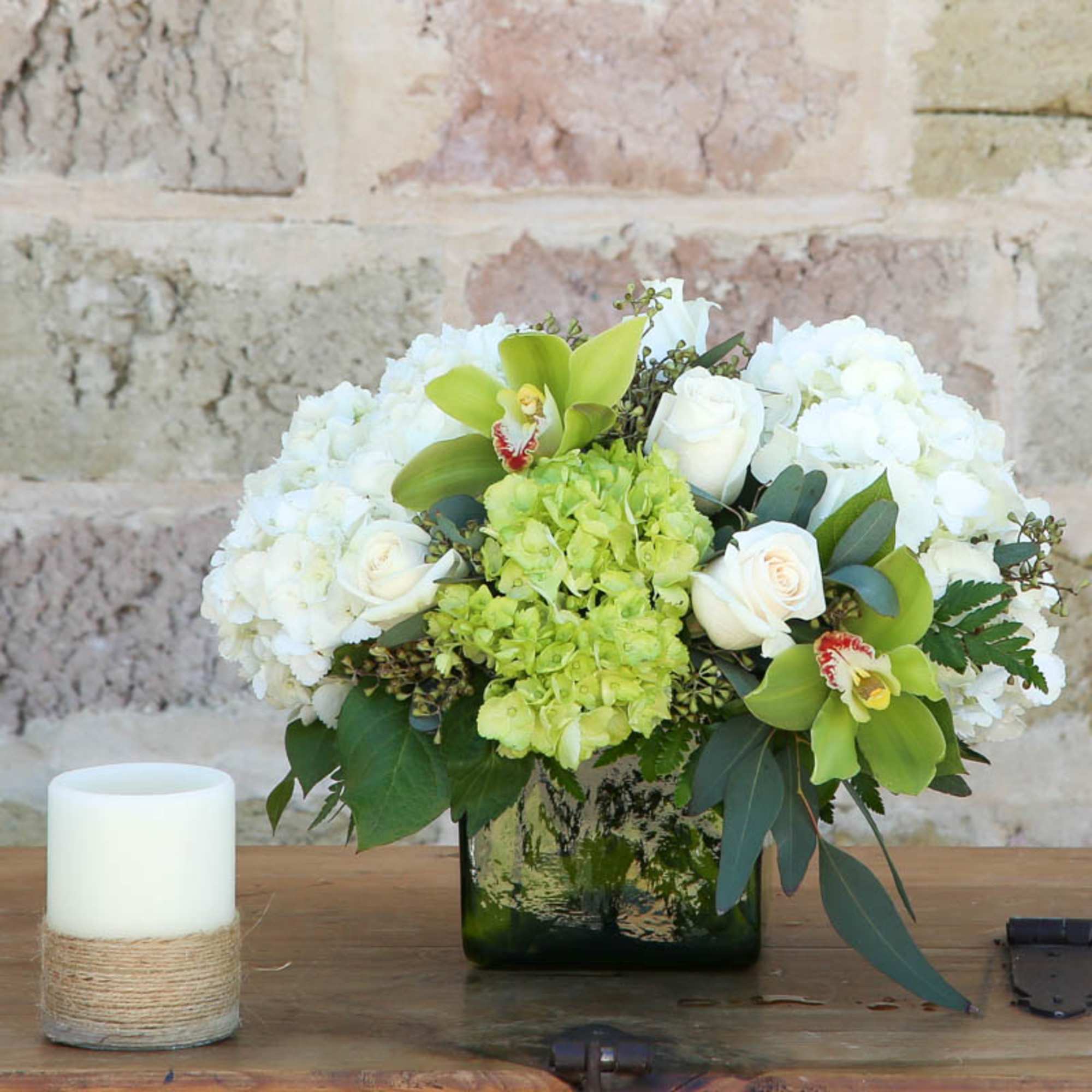 White and green floral arrangement in a dark glass vase beside a white candle