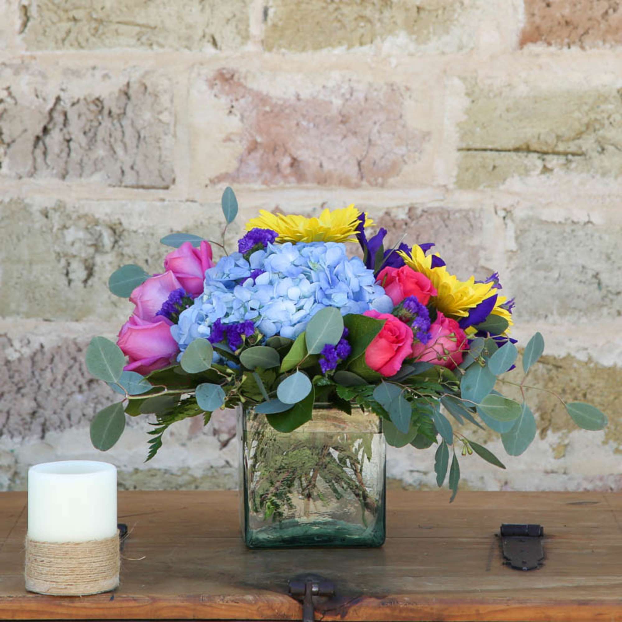 Bouquet of blue hydrangea, pink roses, and yellow flowers in a glass vase