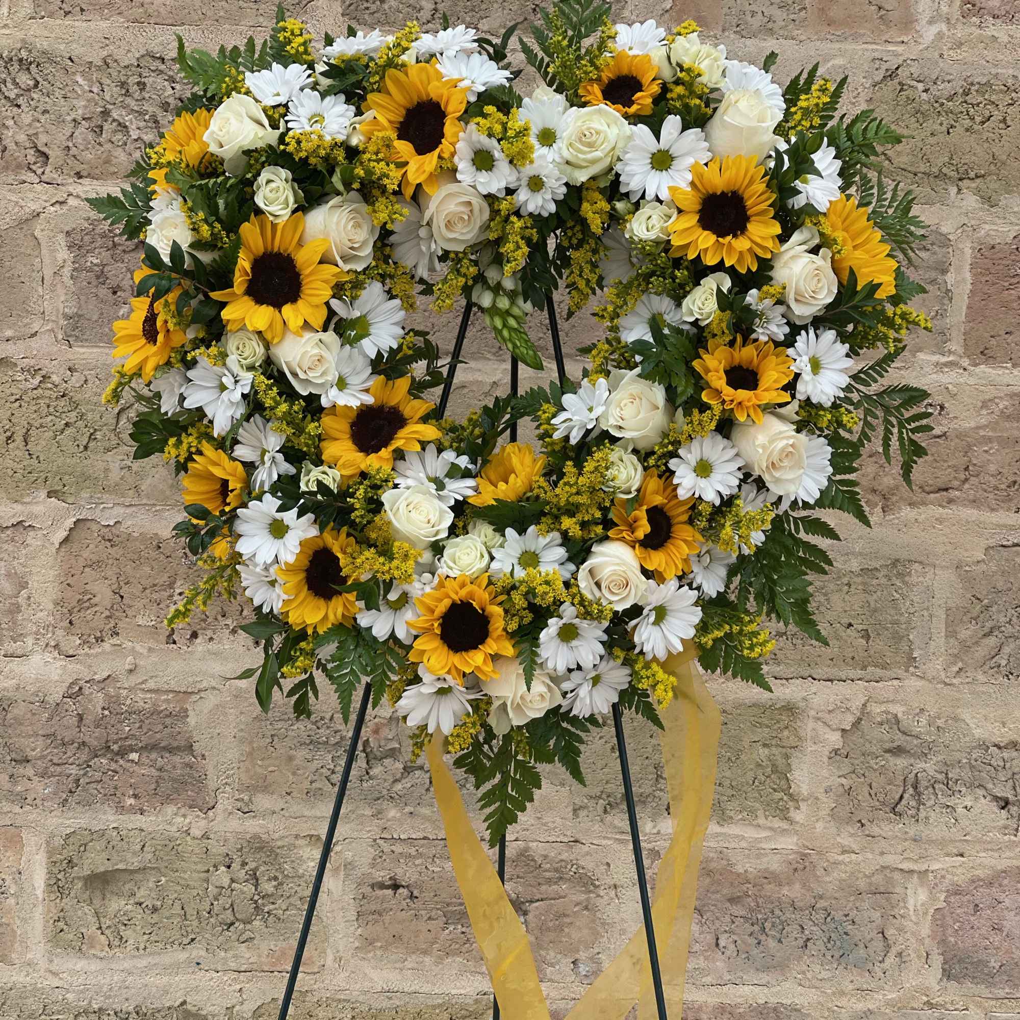 Heart-shaped floral wreath with sunflowers, white roses, and daisies on a stand