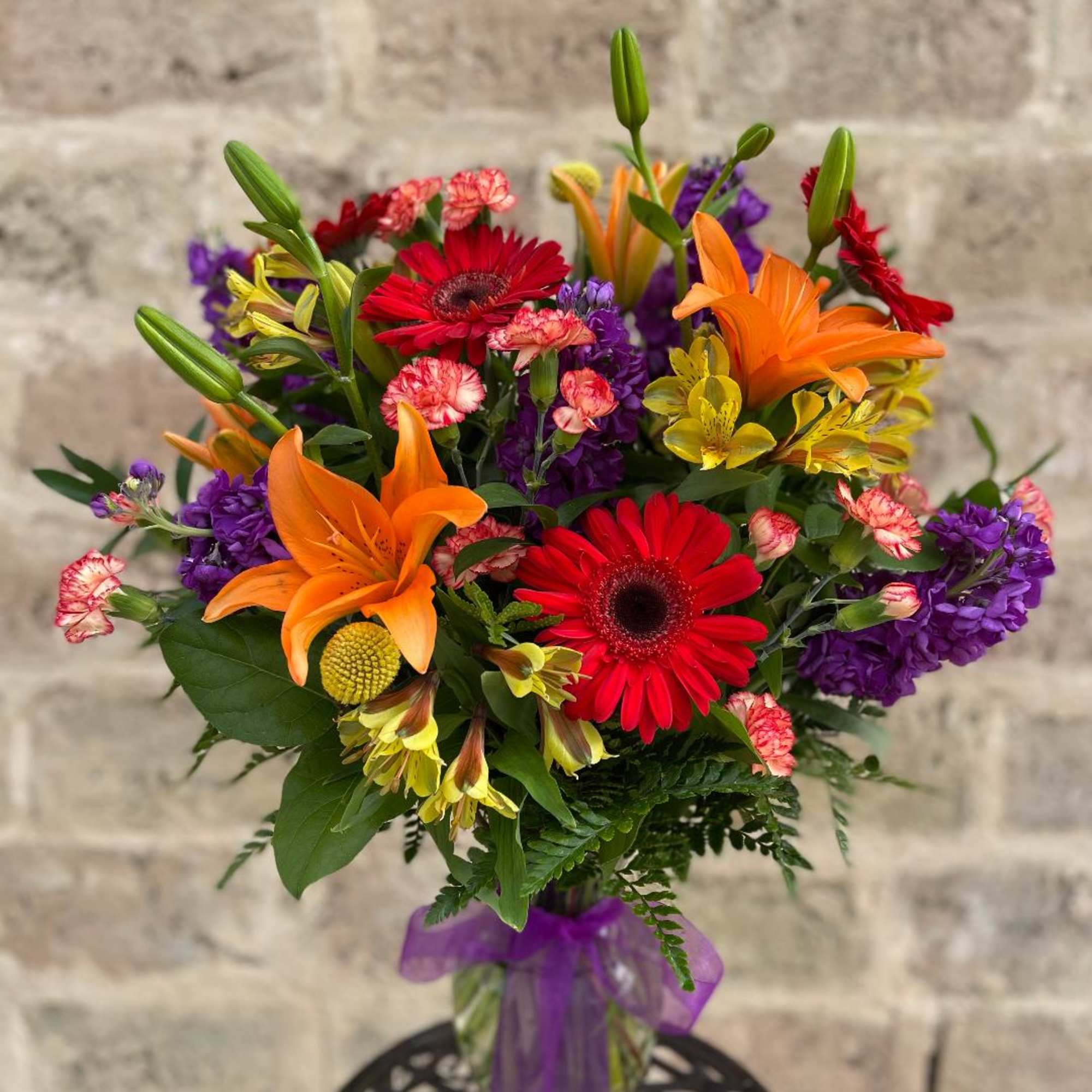 Colorful bouquet with orange lilies, red gerberas, and purple flowers in a vase