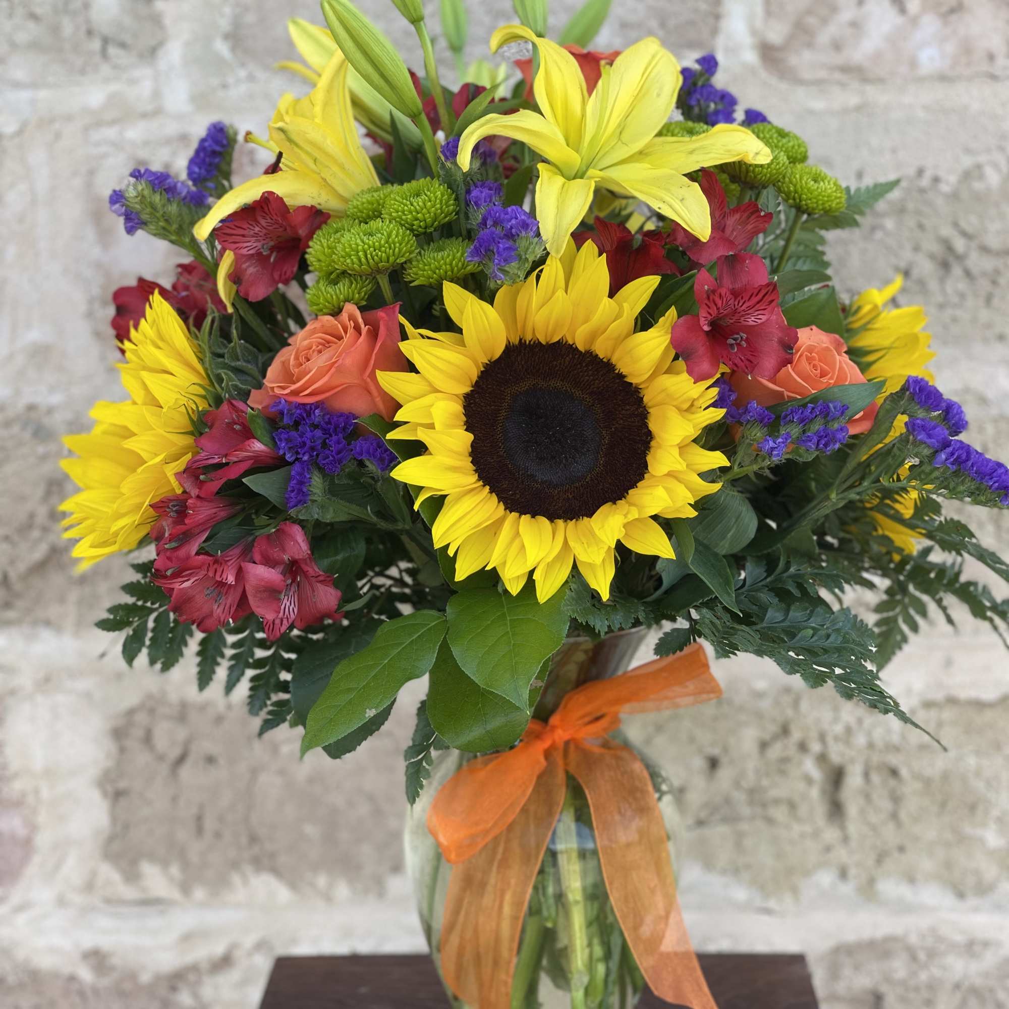 Bouquet of sunflowers, lilies, roses, and purple filler in a glass vase