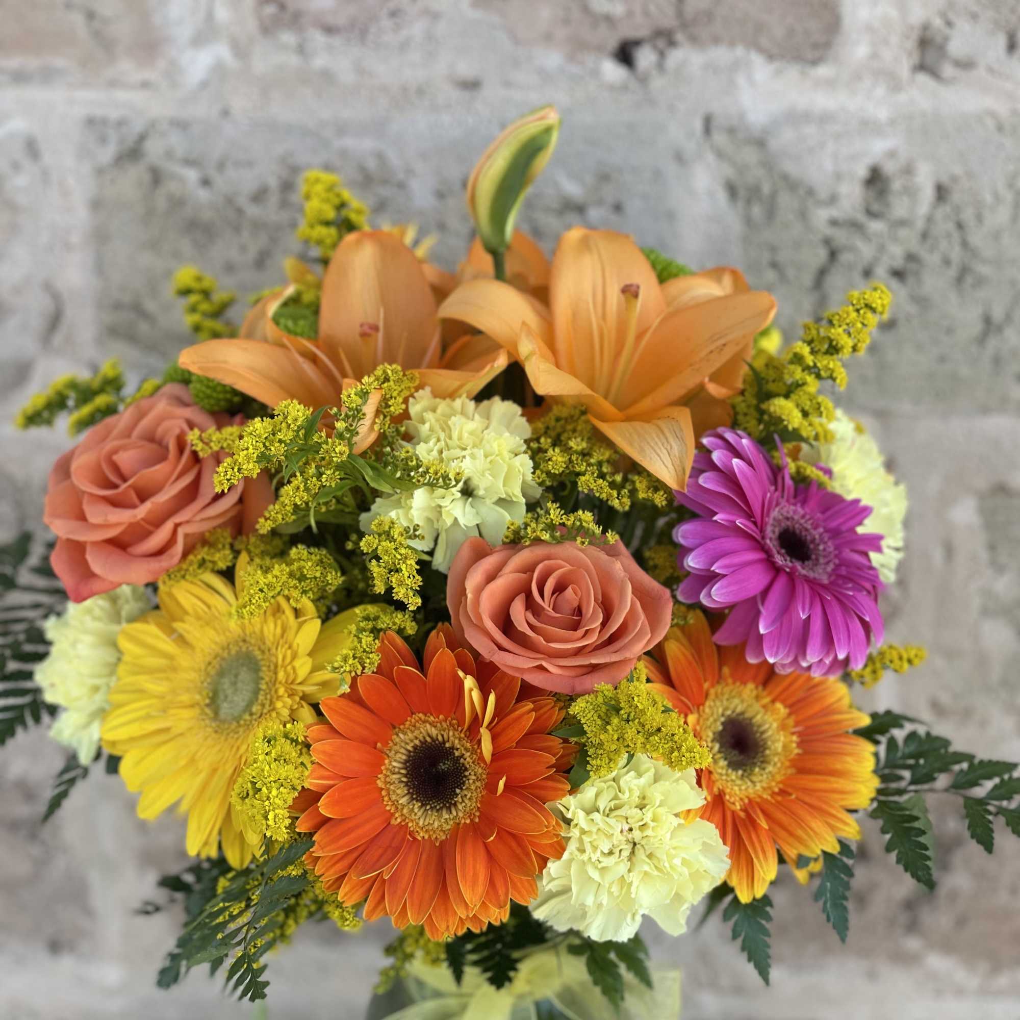 Bouquet of orange lilies, gerbera daisies, and roses in a glass vase