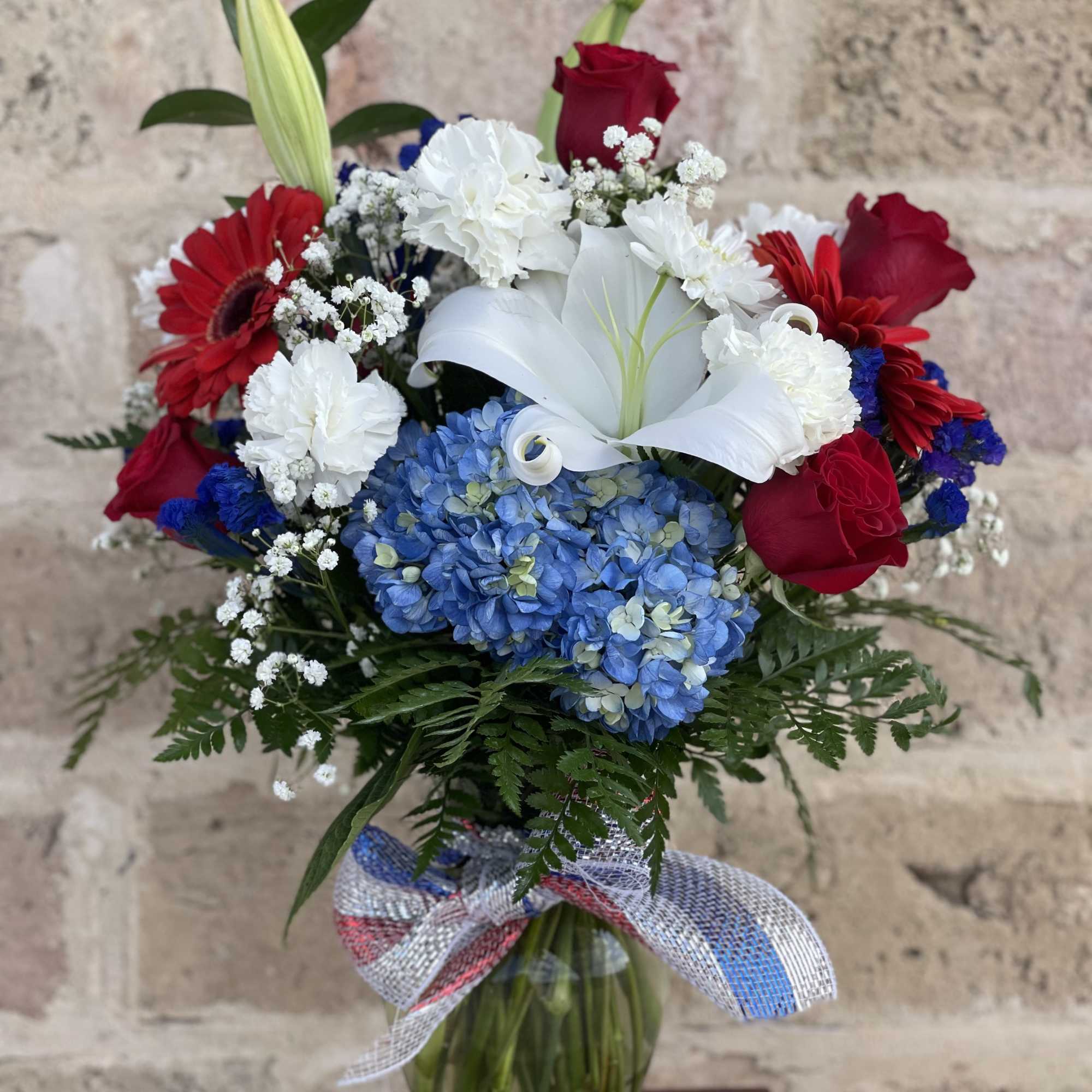Bouquet of red roses, white lilies, and blue hydrangeas in a glass vase