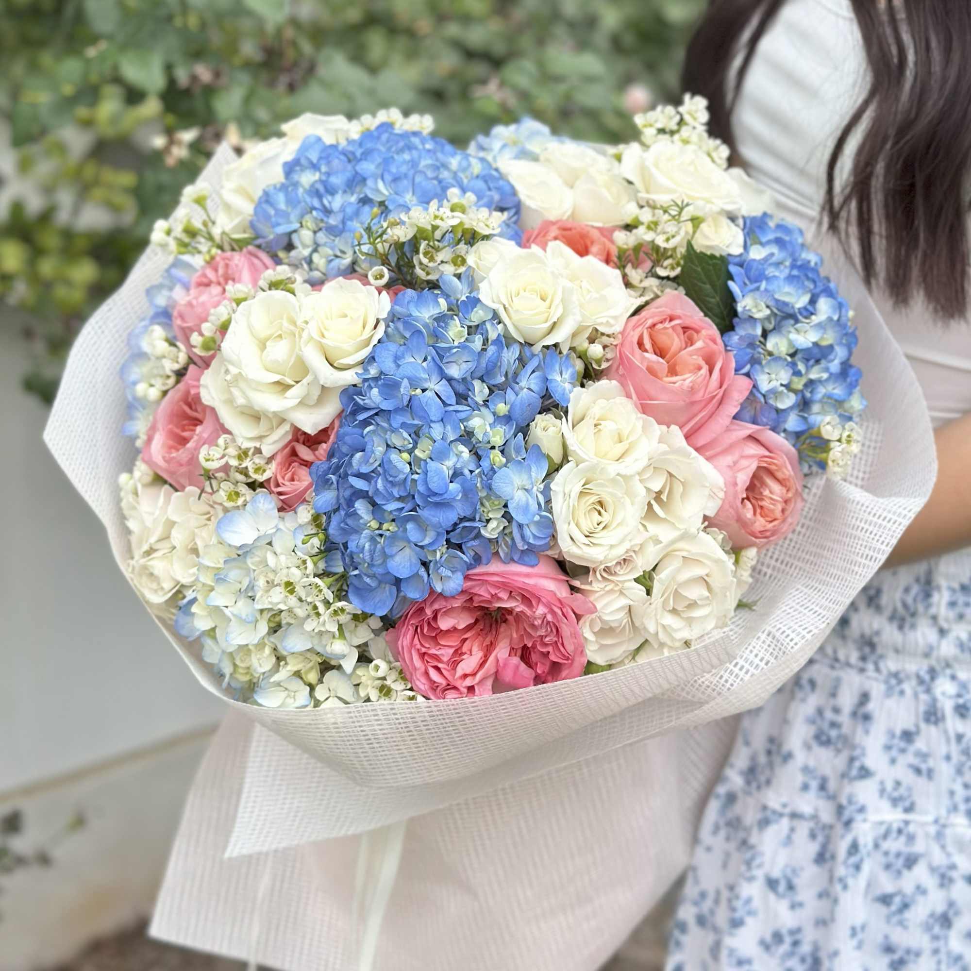 Bouquet of blue hydrangeas and pink and white roses wrapped in pale paper
