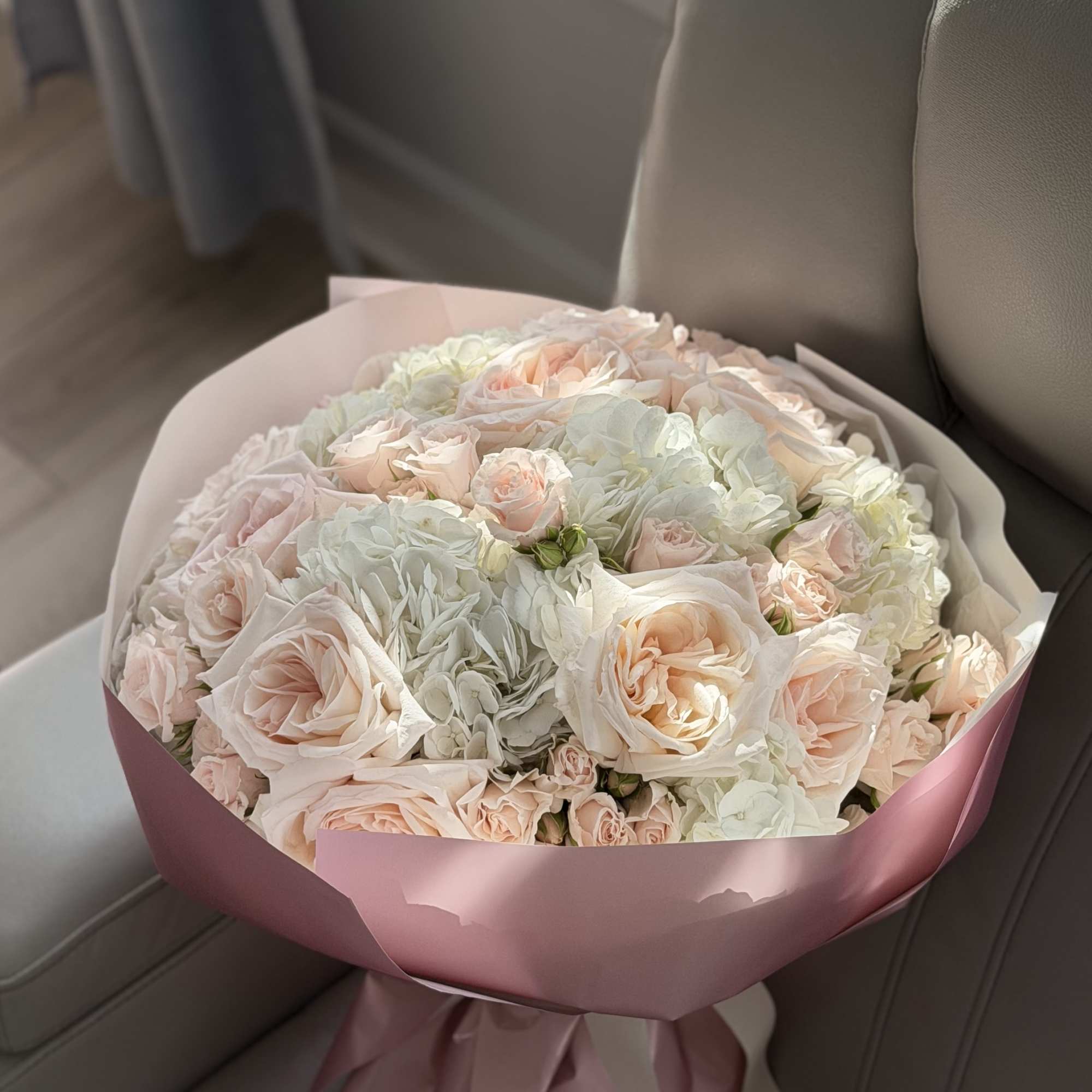 Bouquet of pale pink roses and white hydrangeas wrapped in pink paper