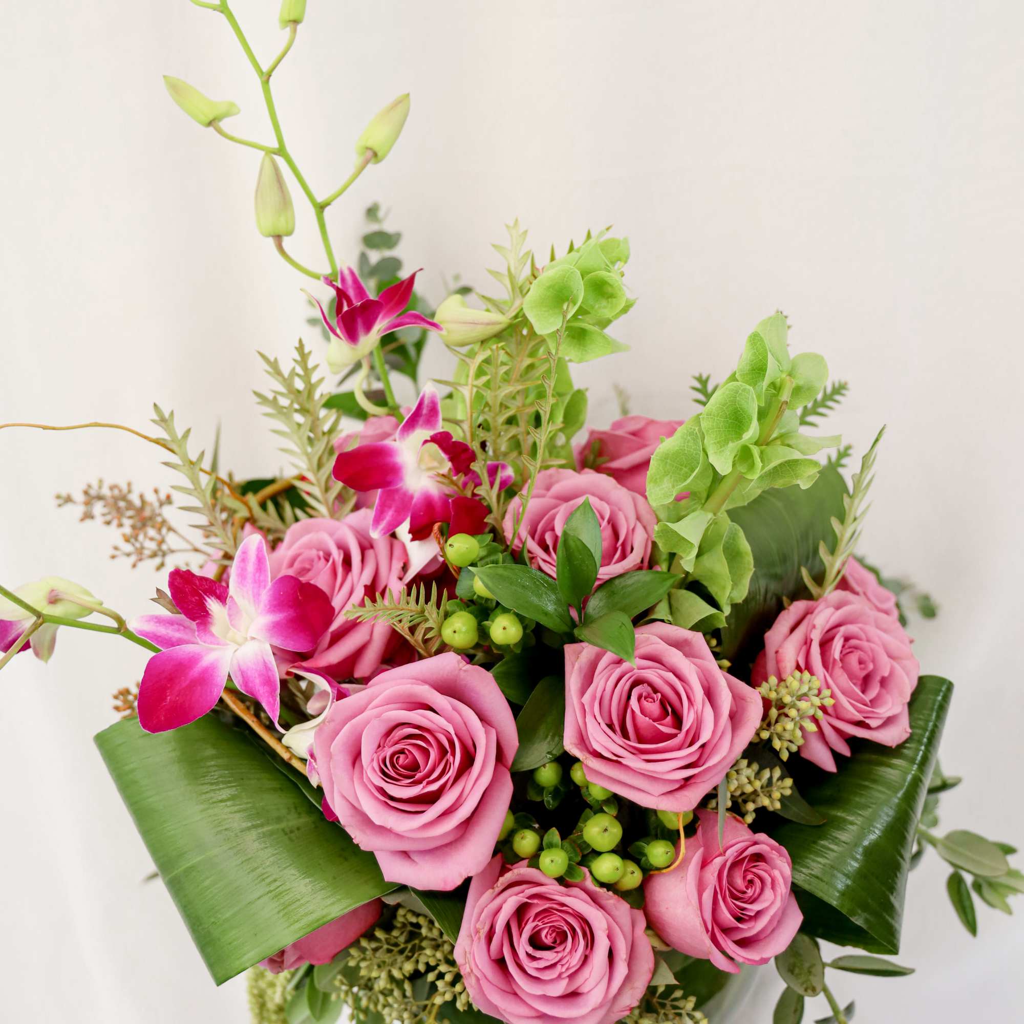 Pink roses and orchids arranged in a low bouquet with green foliage