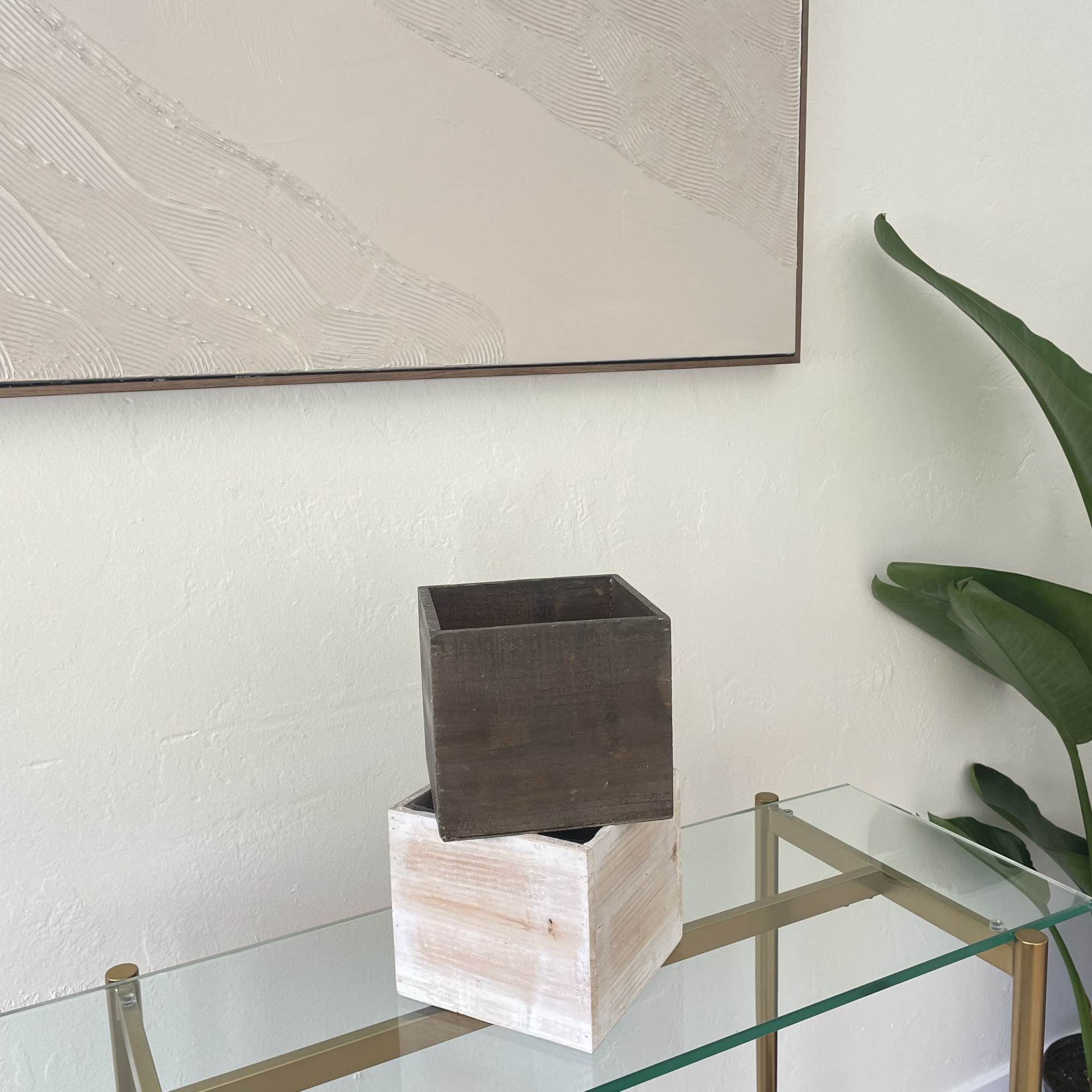 Two empty wooden cube planters stacked on a glass table.