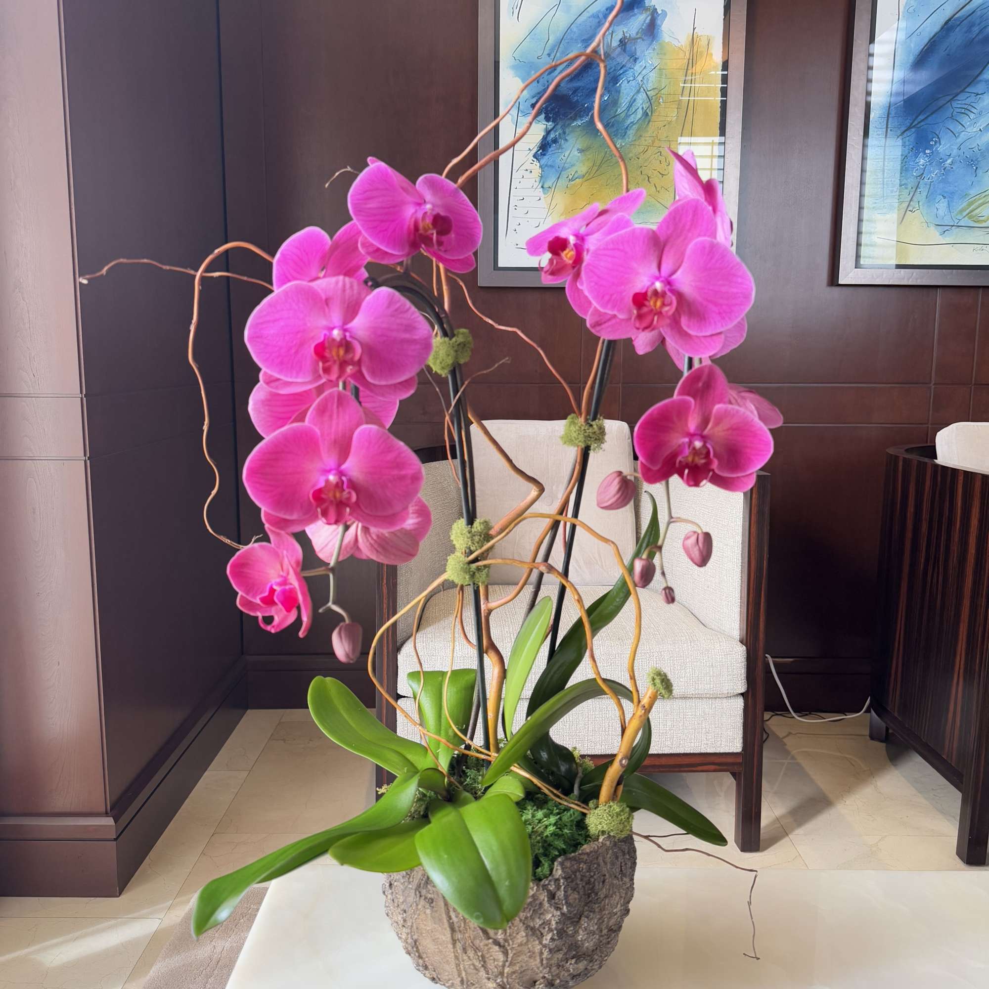 Pink orchids arranged in a decorative planter with twisting branches.