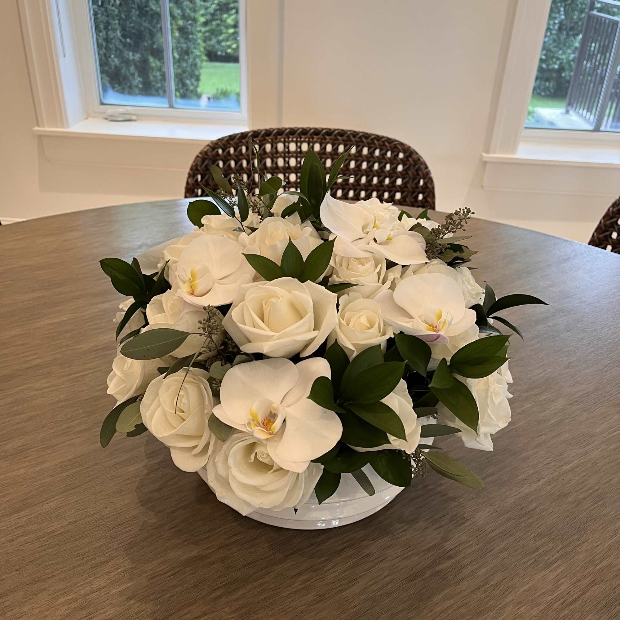 White roses and orchids arranged in a low white bowl