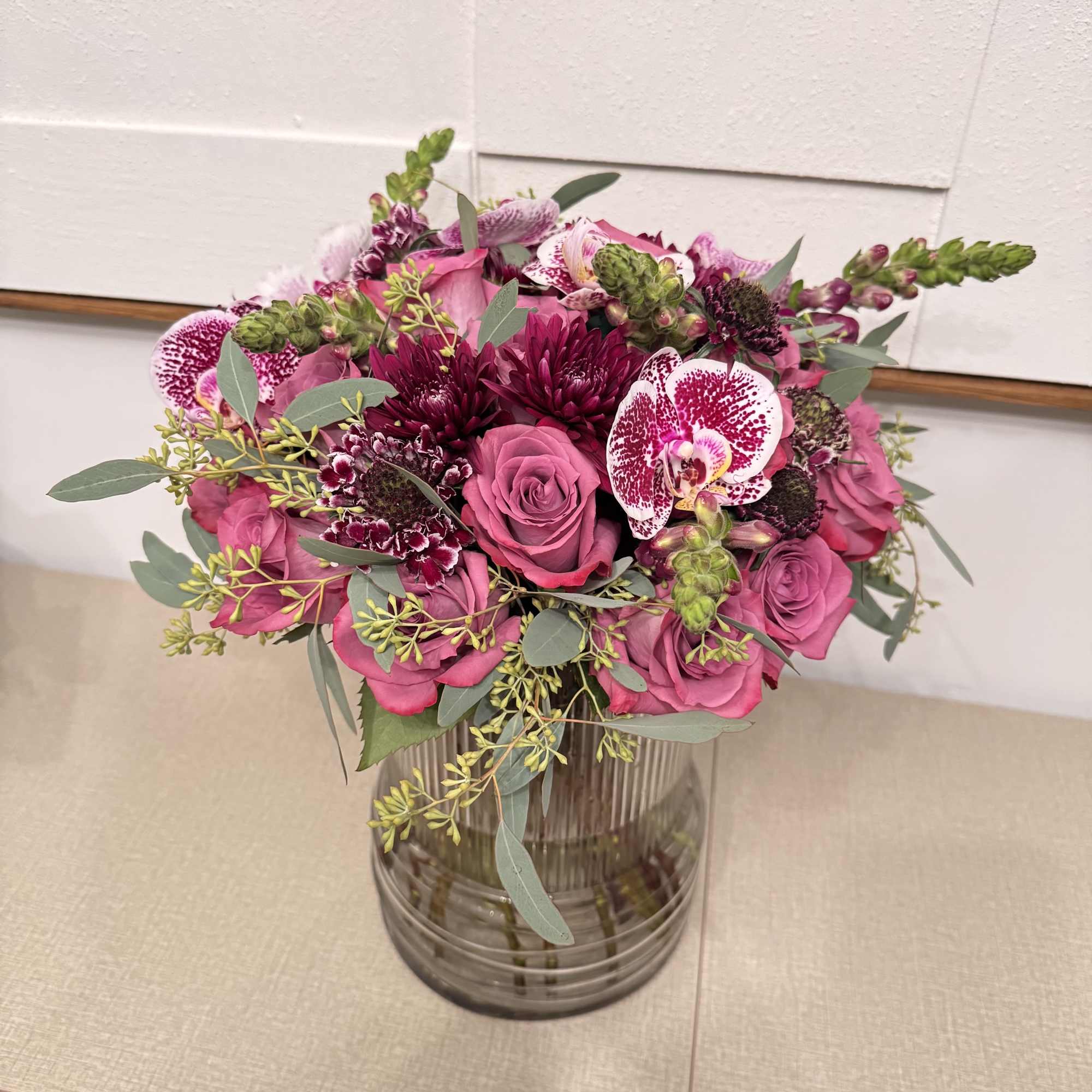 Pink rose bouquet with orchids and dark blooms in a glass vase