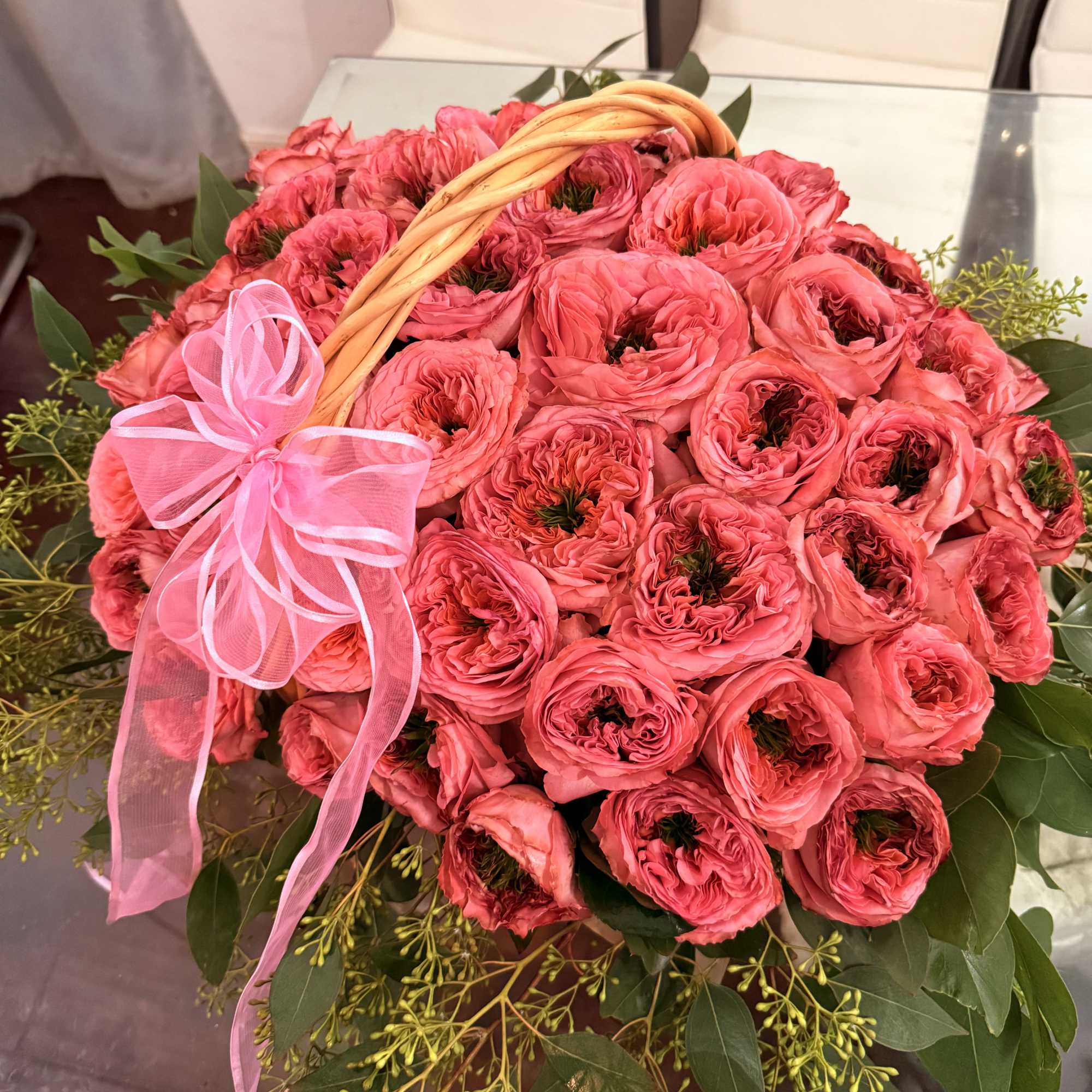 Basket of pink ranunculus with a pink ribbon and greenery