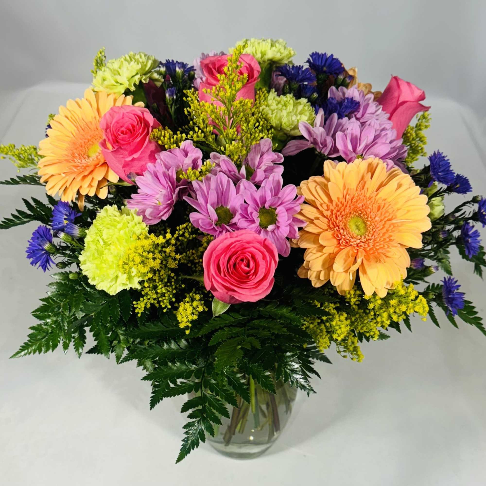 Mixed bouquet of pink, purple, yellow, and orange flowers in a glass vase