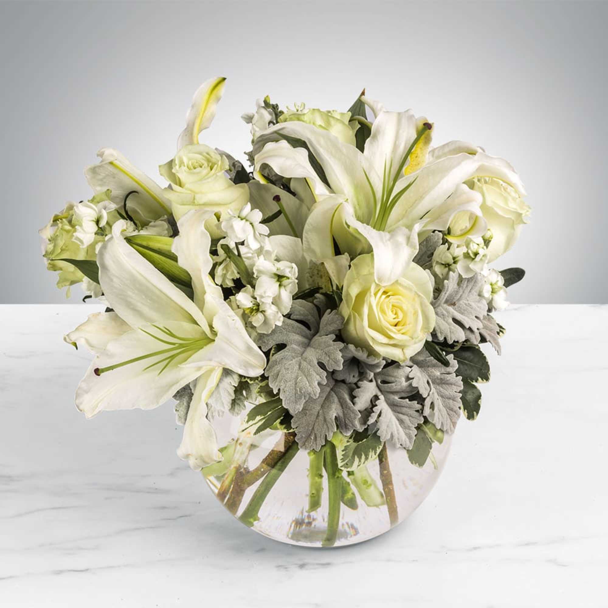 This arrangement includes white roses, white asiatic lilies, white stock, and dusty