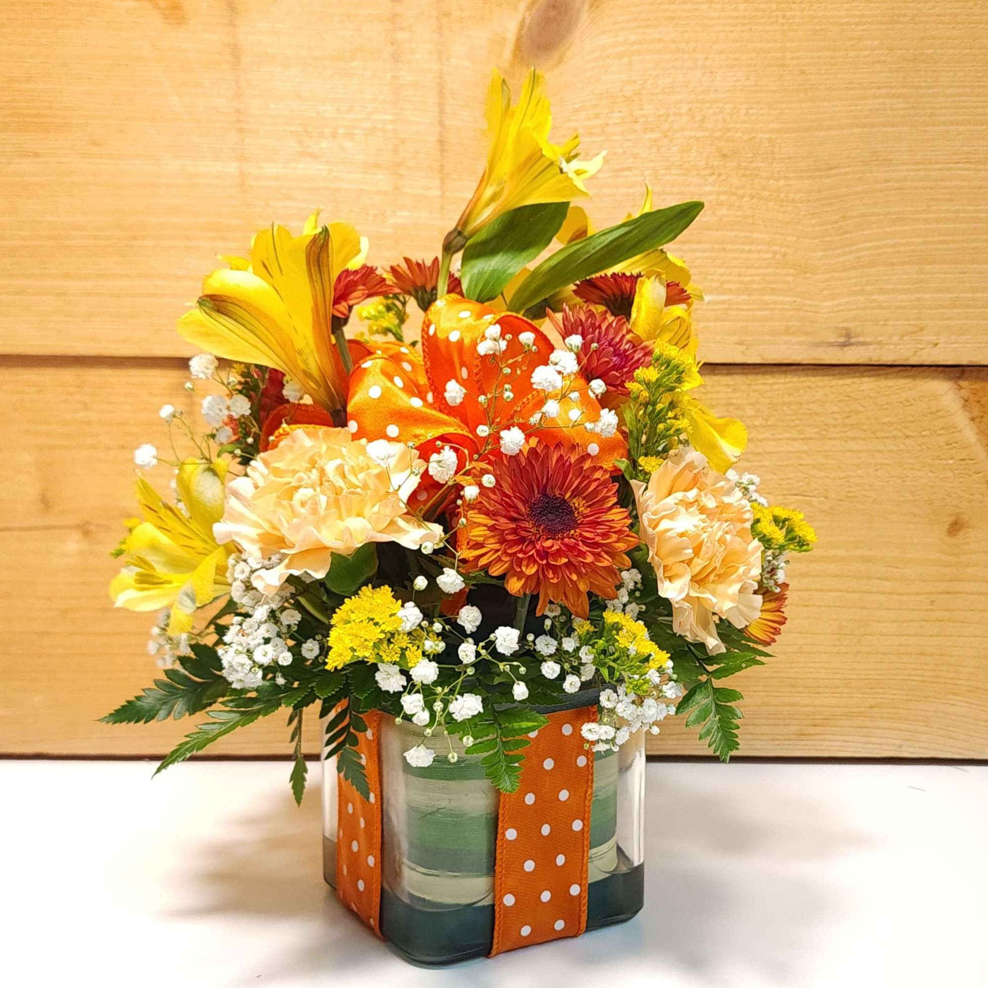 Orange and yellow floral arrangement in a glass vase with polka-dot ribbon