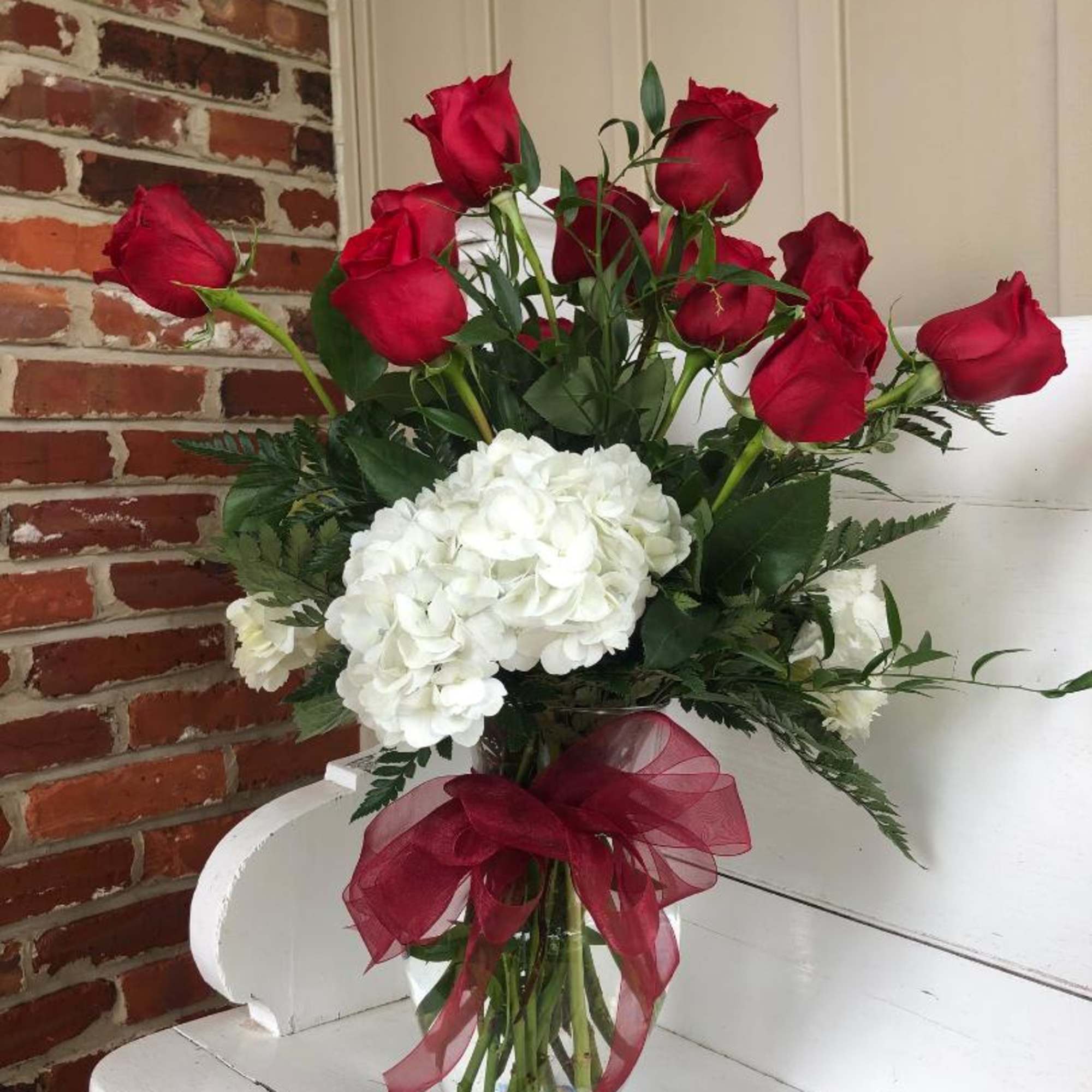Bouquet of red roses and white hydrangeas in a glass vase with a burgundy ribbon