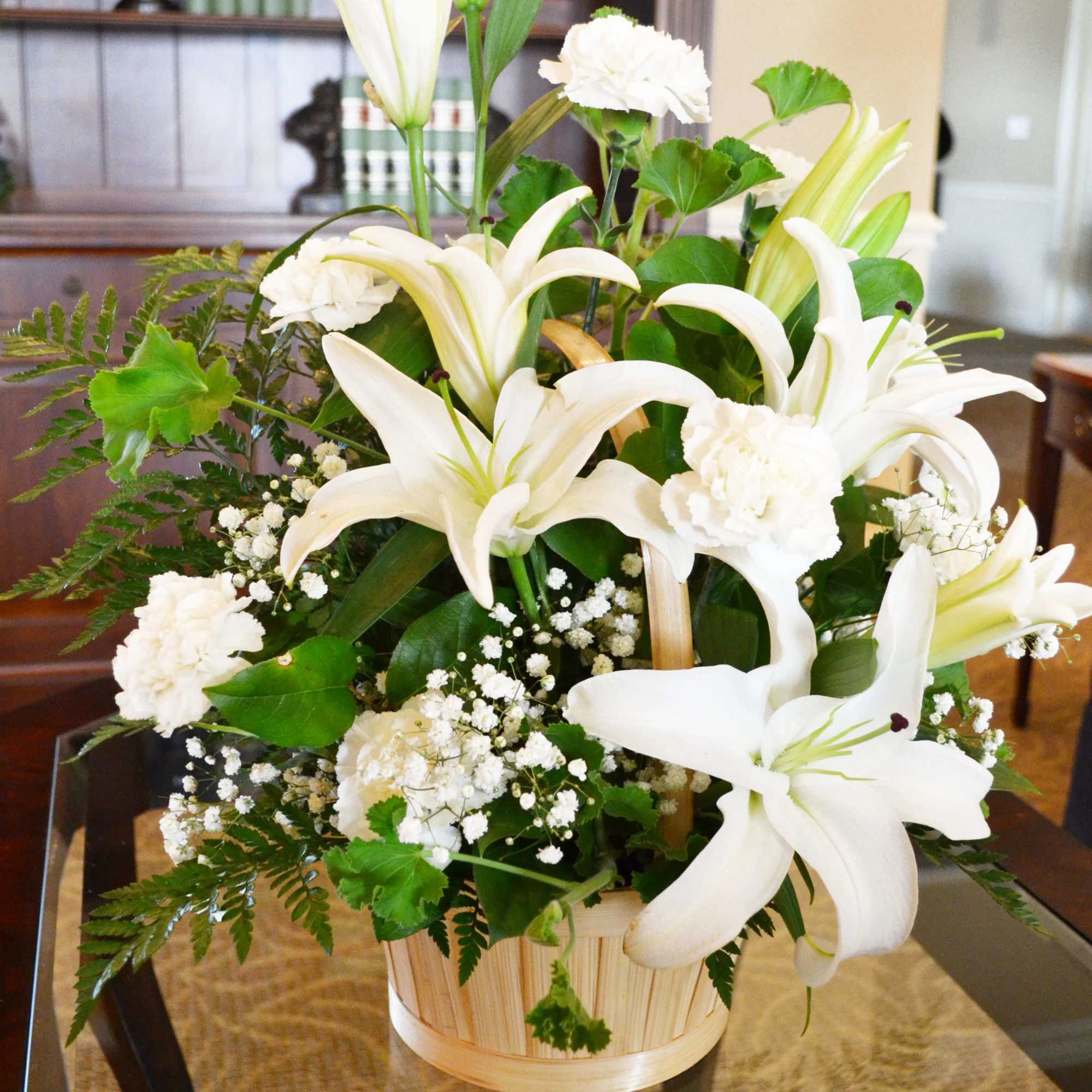 Table basket arrangement filled with Lilies, Carnations, Baby's Breath, and Mixed Greens