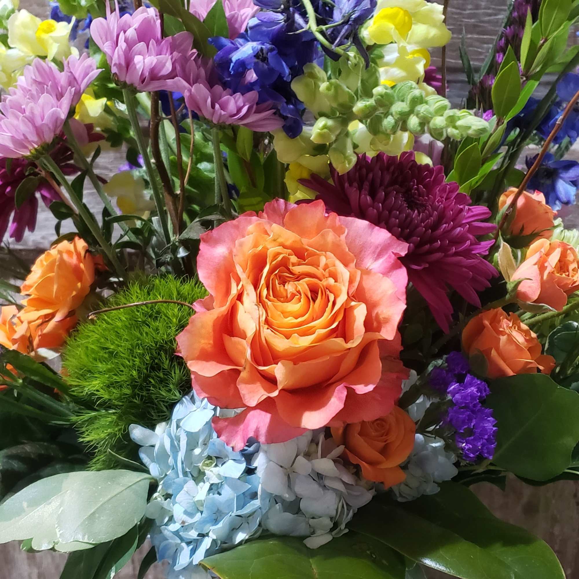 Mixed bouquet with orange roses, purple blooms, and yellow snapdragons in a glass vase