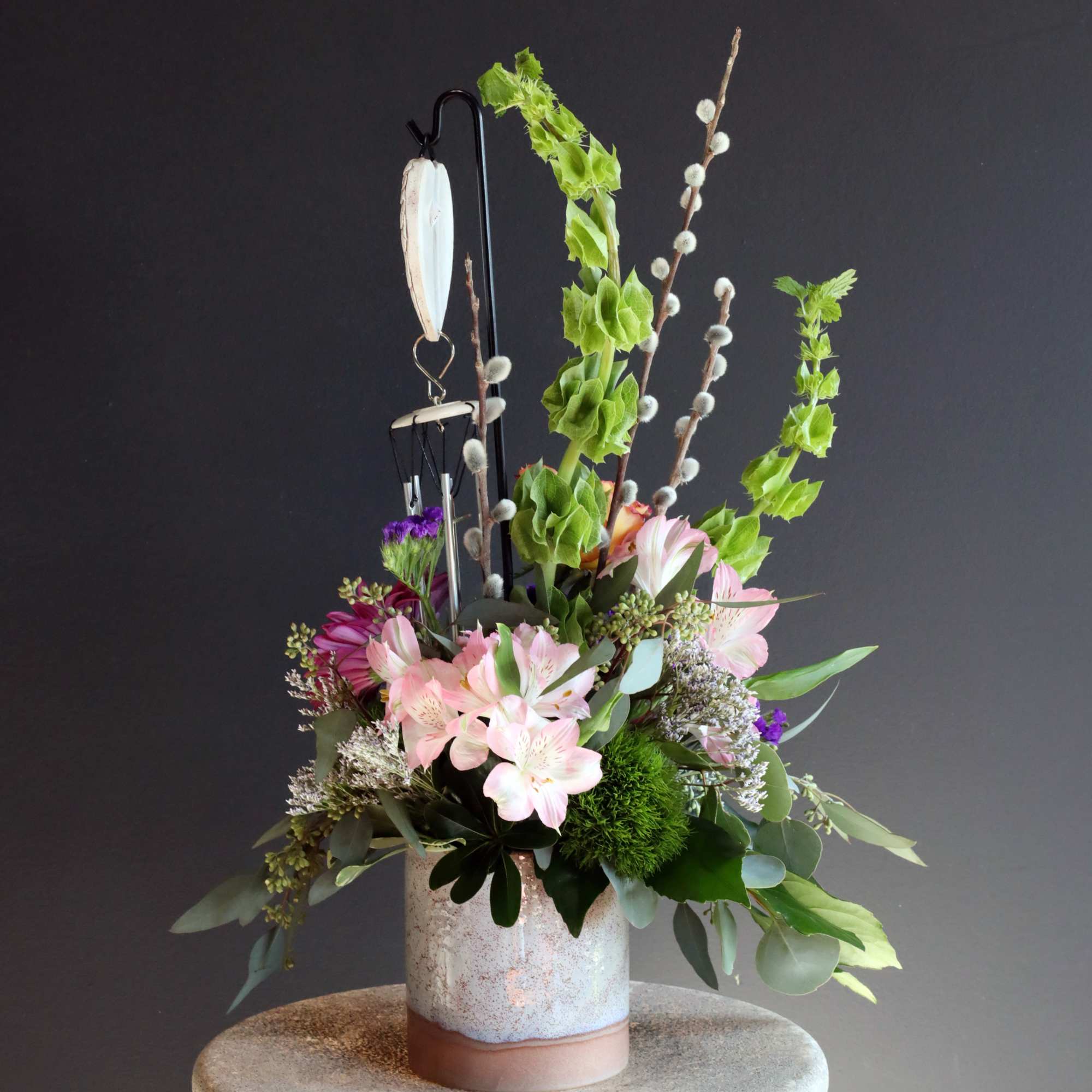 A gorgeous sympathy arrangement with a small hanging wind chime keepsake with