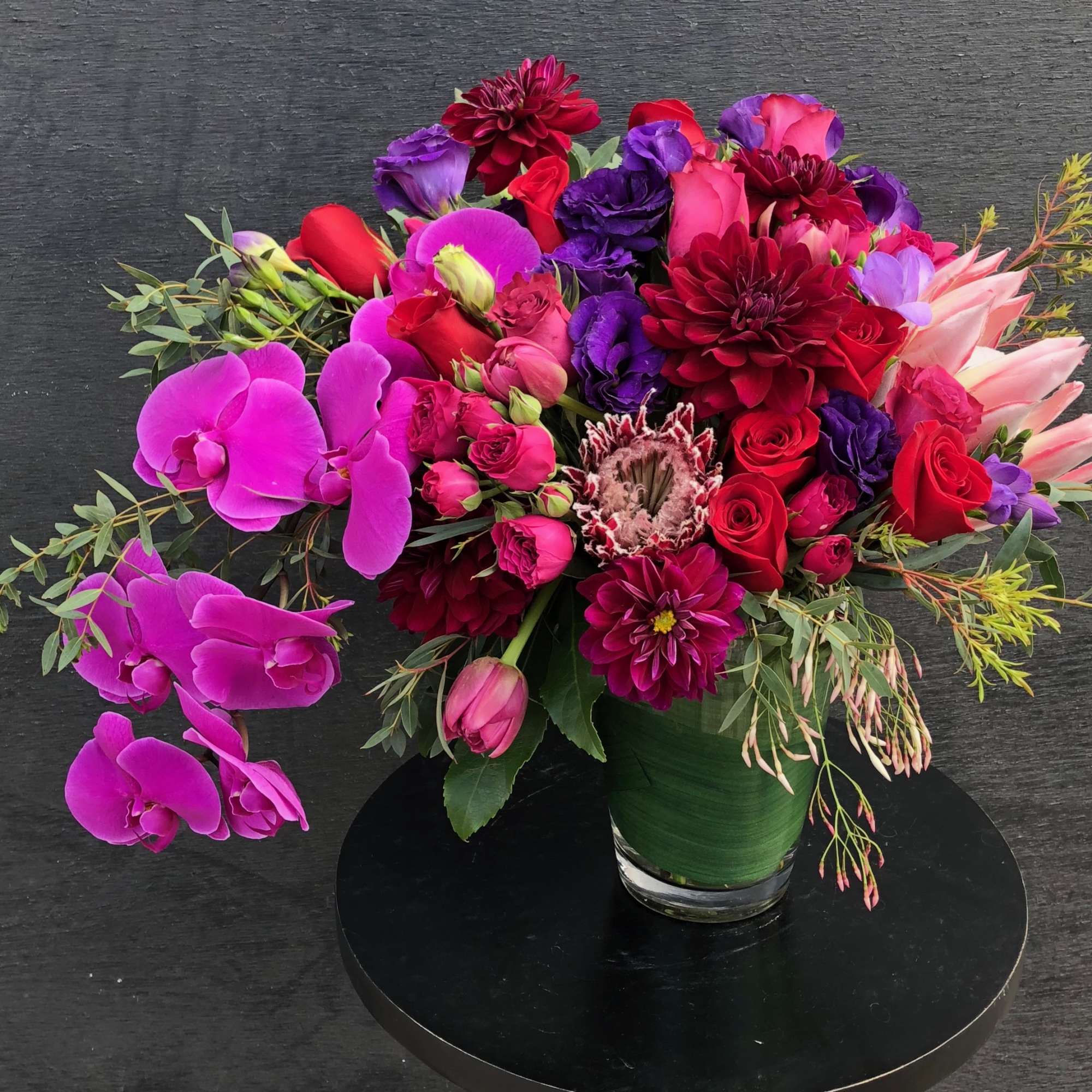 Bright mixed bouquet with orchids, roses, and dahlias in a glass vase