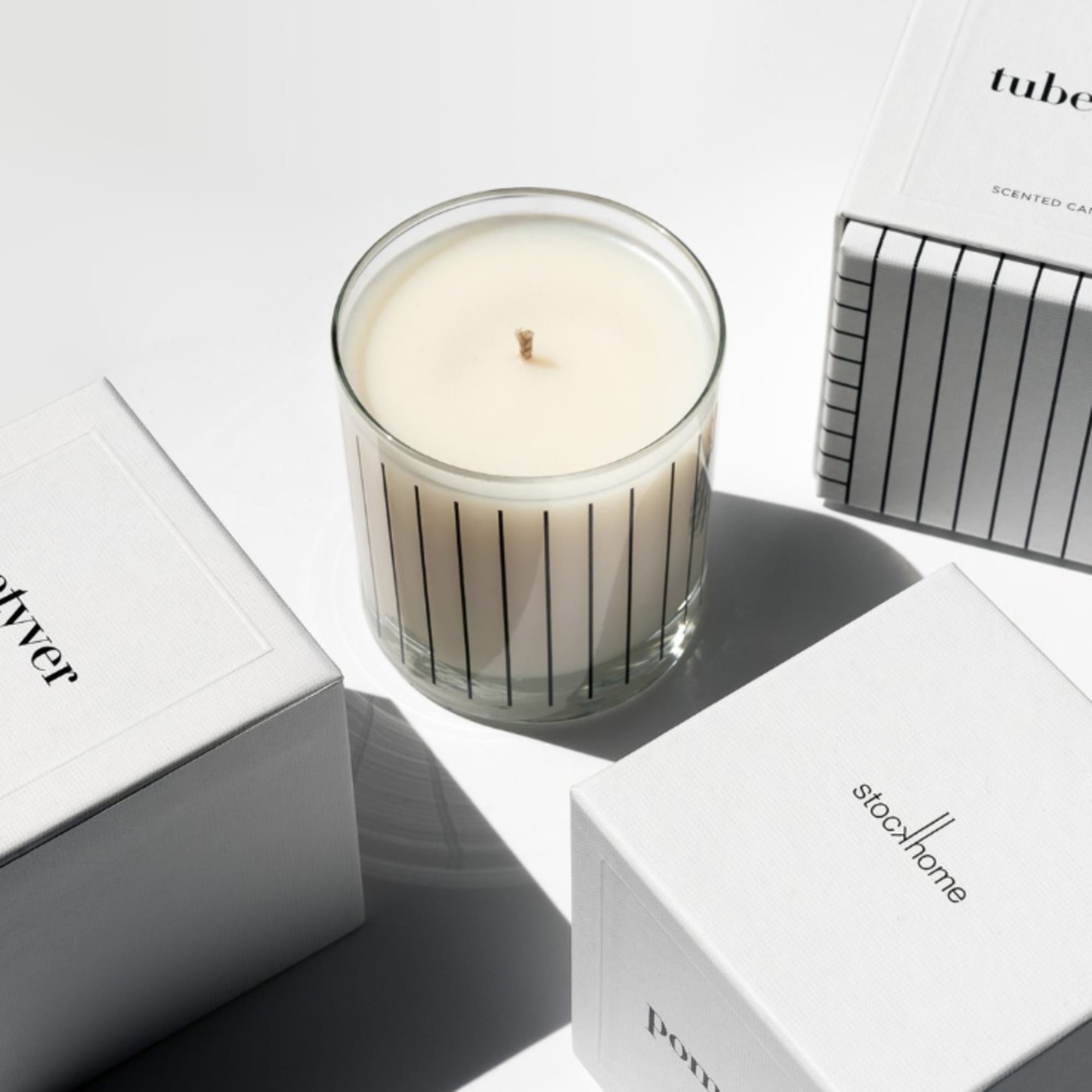 A scented candle in a glass jar surrounded by white product boxes