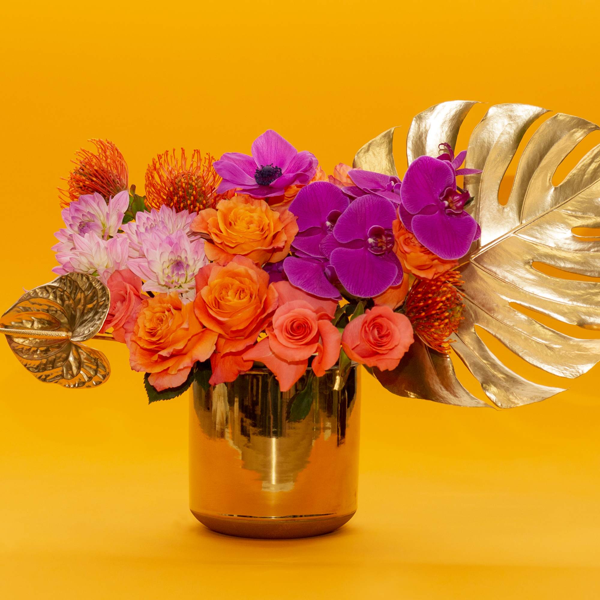 Bright mixed bouquet in a gold vase with large metallic leaves