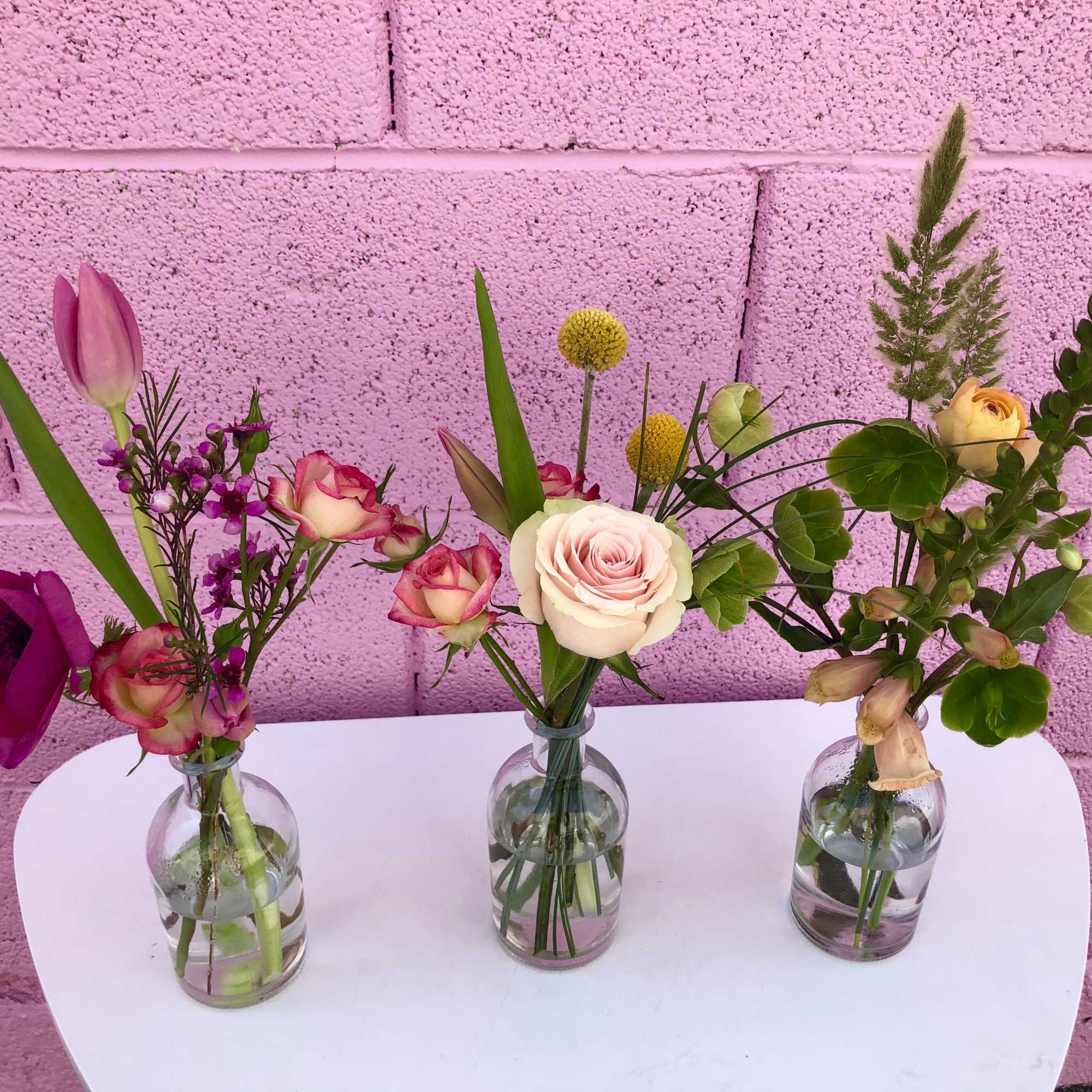 Three small floral arrangements in glass bottles on a white table