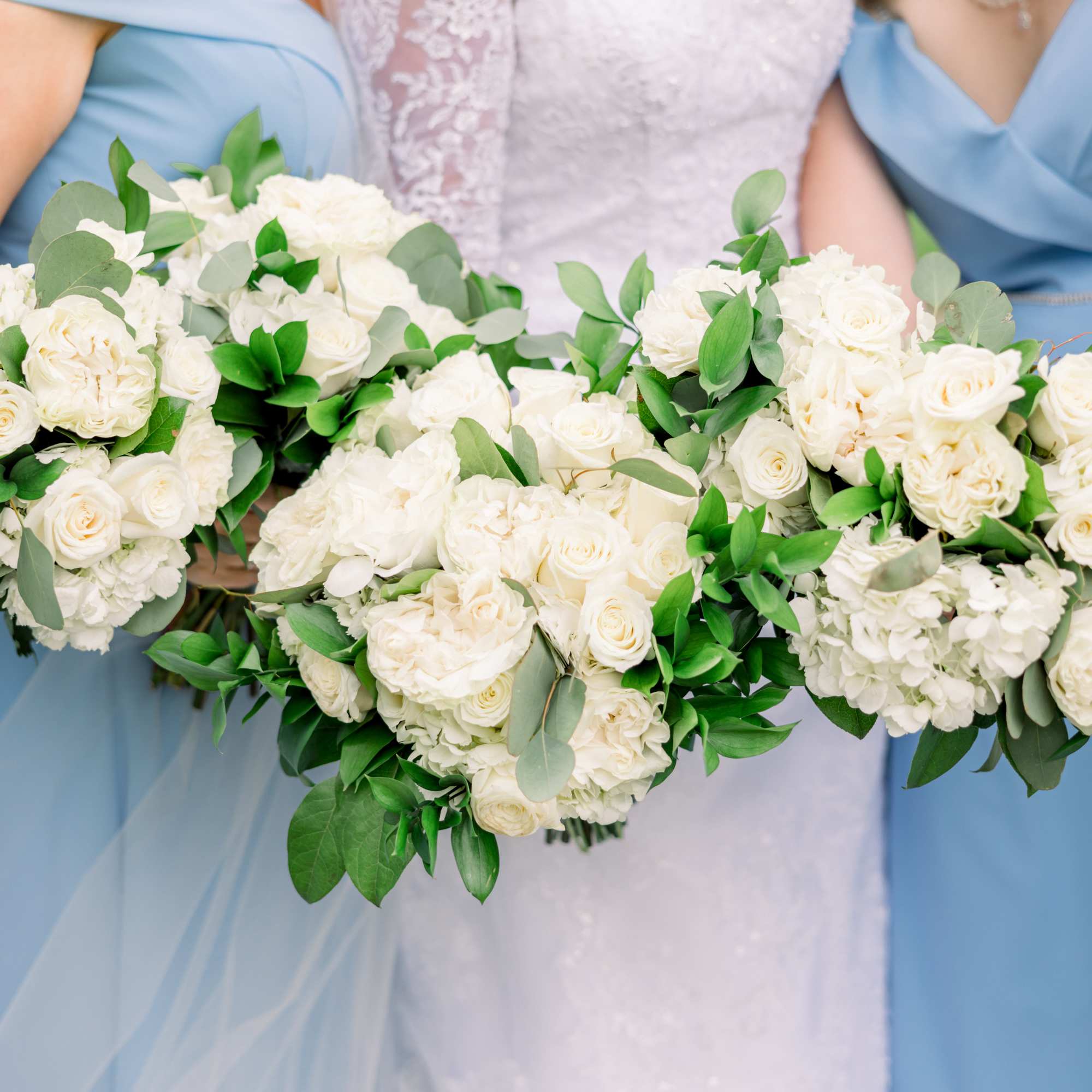 Bridesmaids holding white rose bouquets with greenery