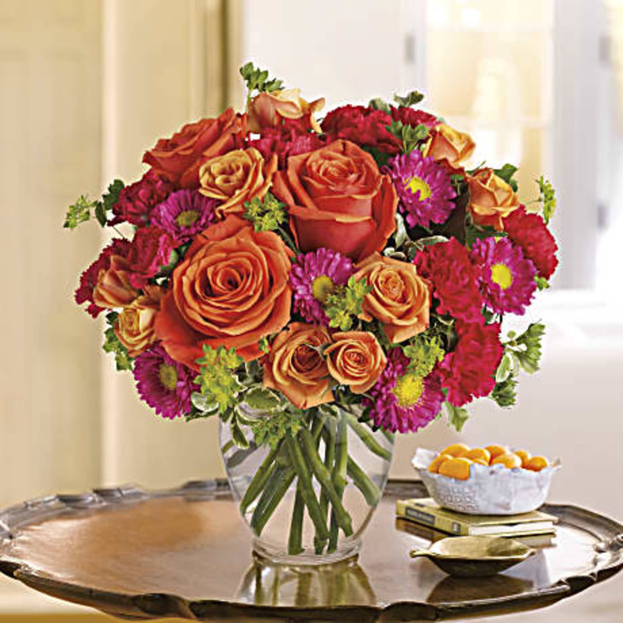 Orange roses and pink daisies in a clear glass vase