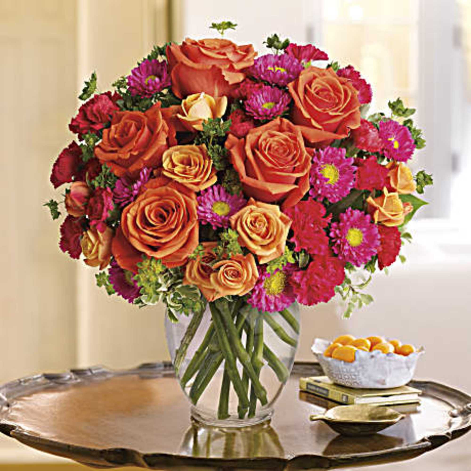 Orange roses and pink daisies in a clear glass vase