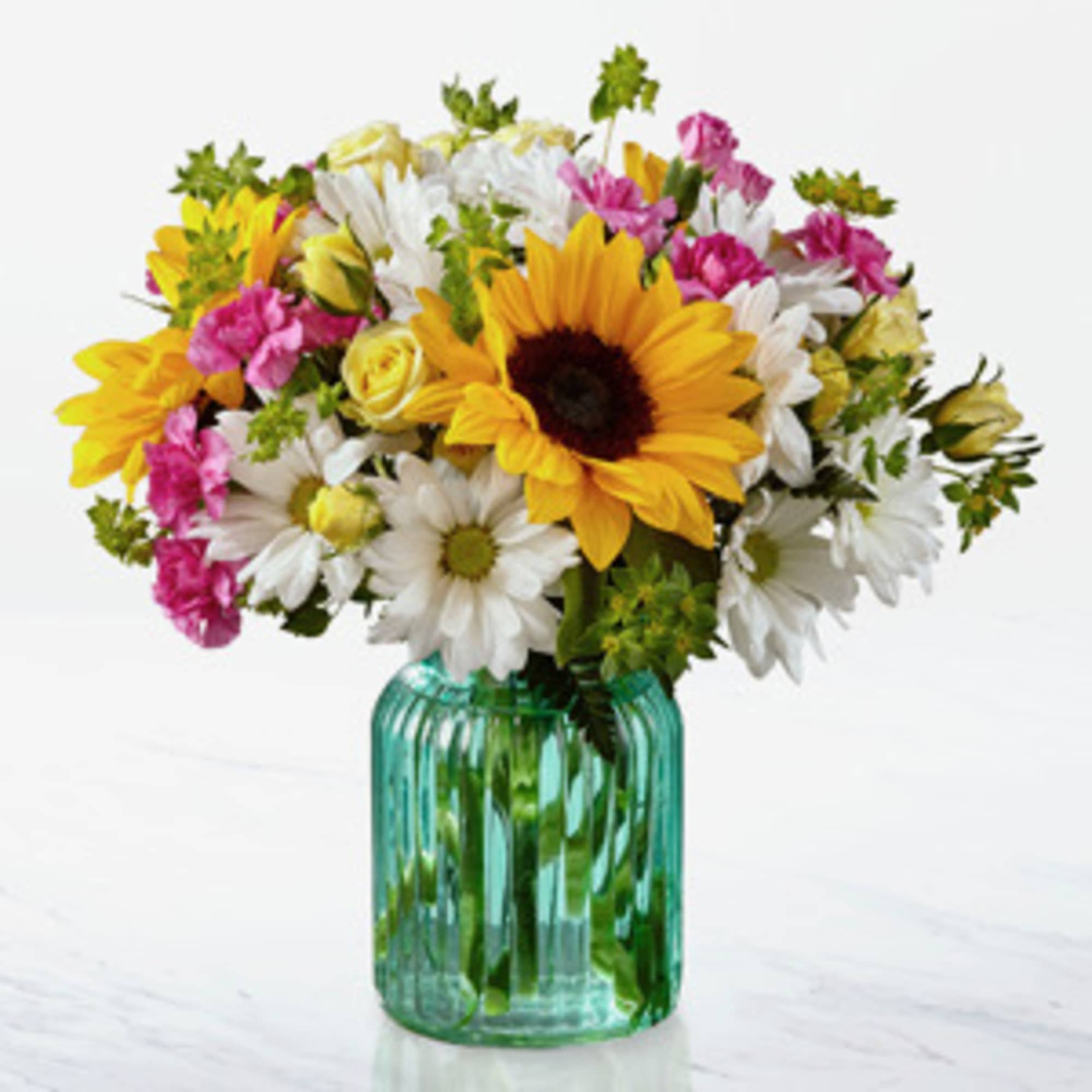 Bouquet of sunflowers, white daisies, and pink carnations in a green glass vase