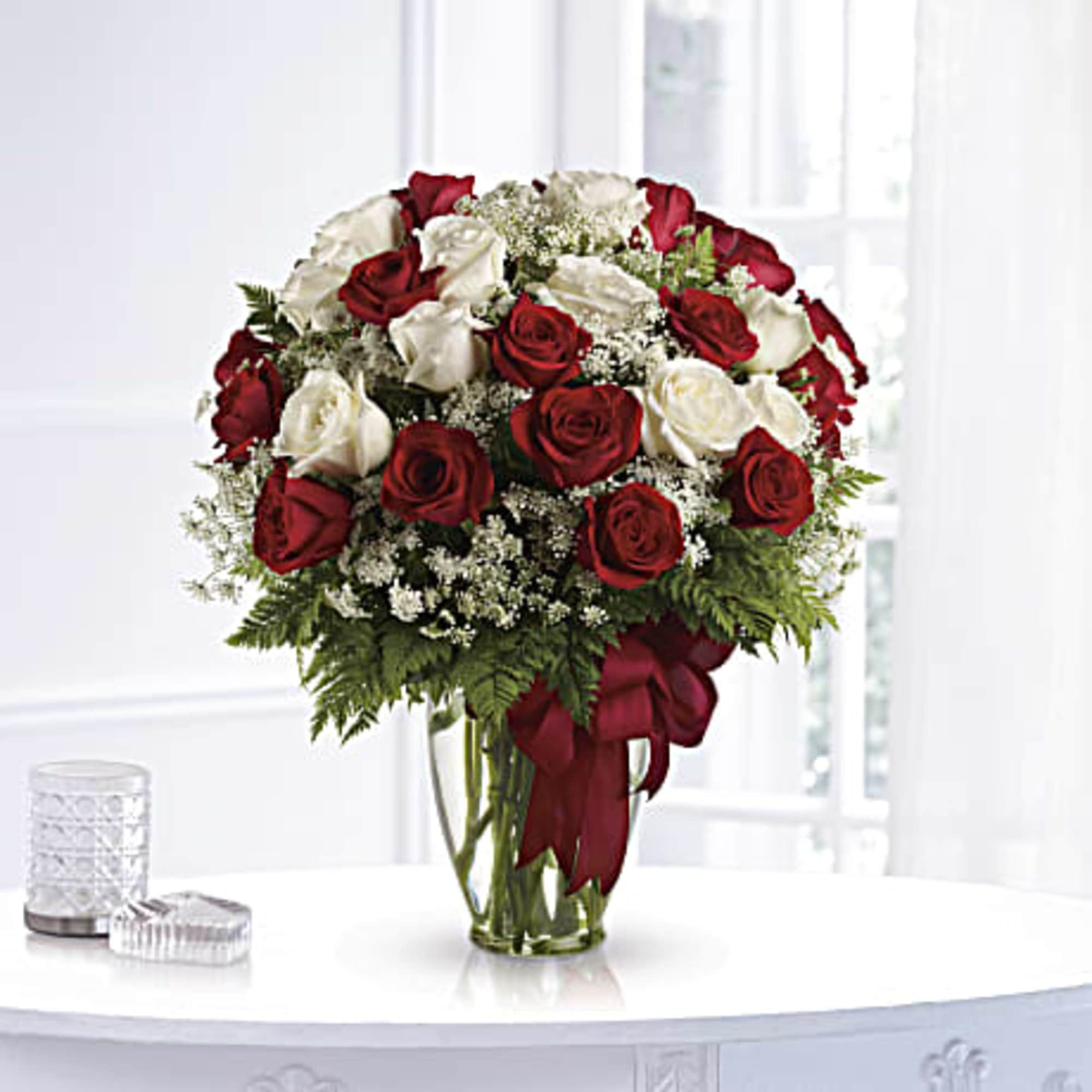 Red and white roses in a clear glass vase with a red ribbon