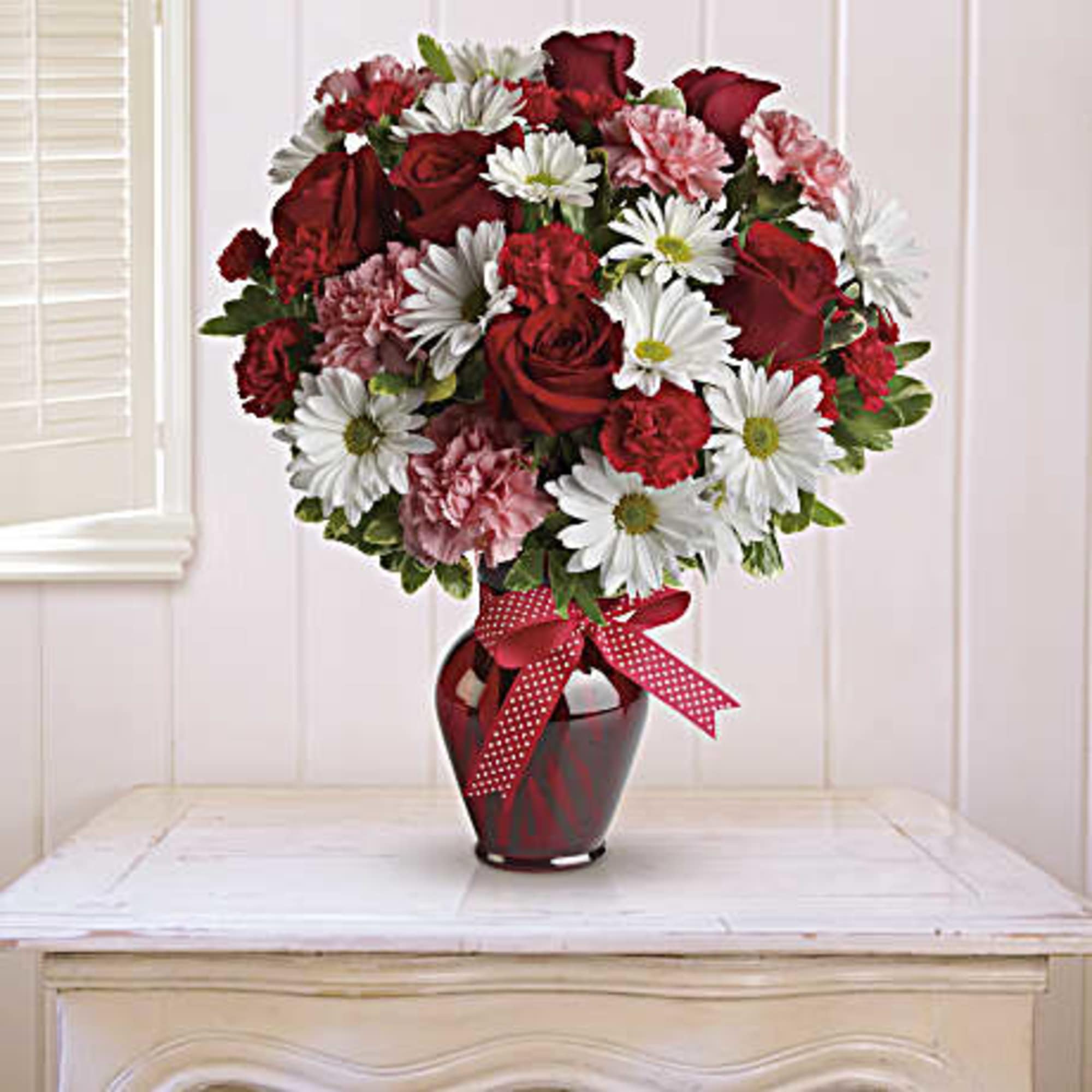 Bouquet of red roses, white daisies, and pink carnations in a red vase