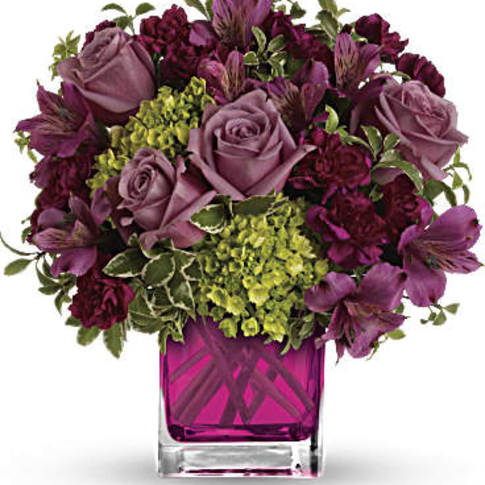 Purple roses and mixed blooms arranged in a pink glass vase
