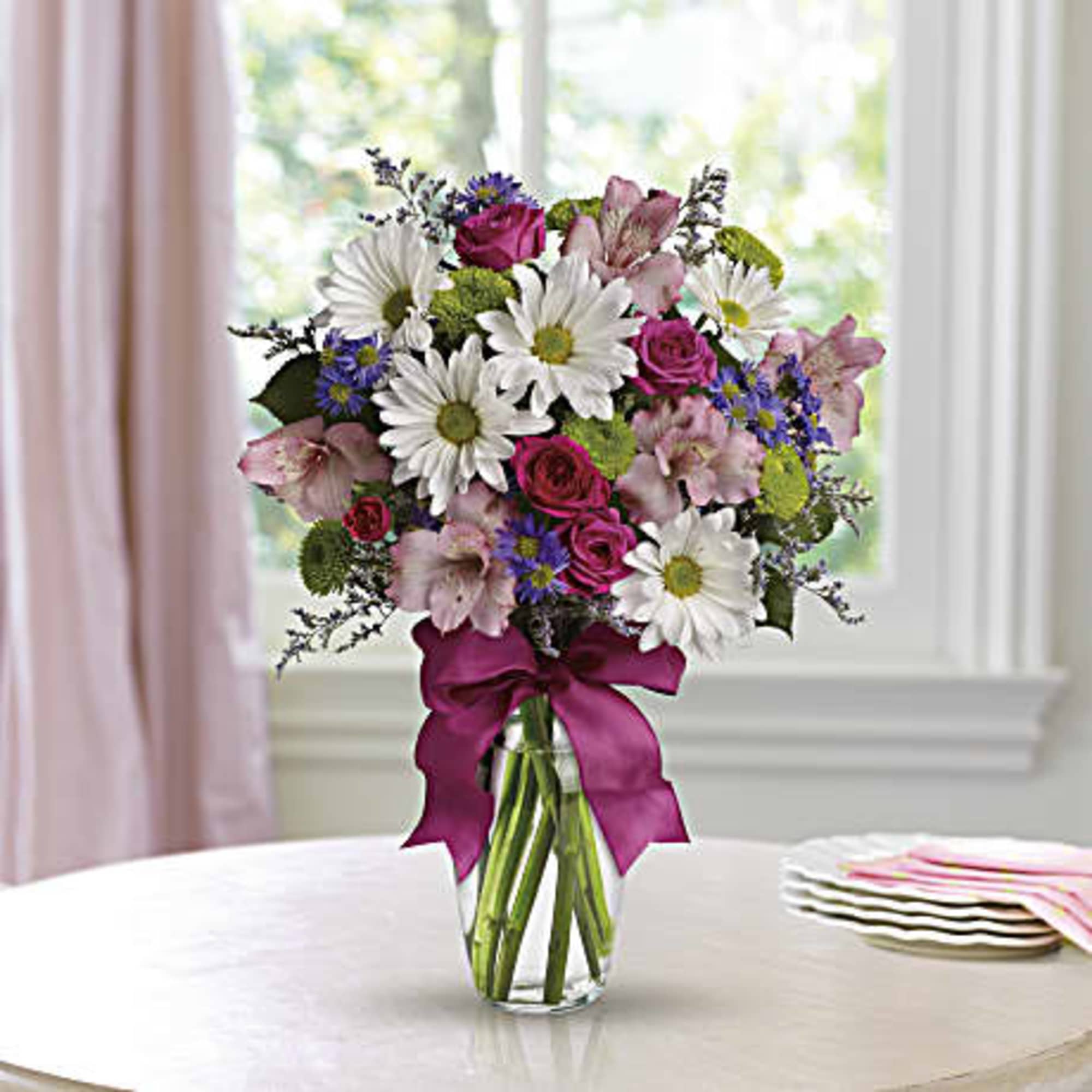 Bouquet of white daisies, pink roses, and pink lilies in a glass vase