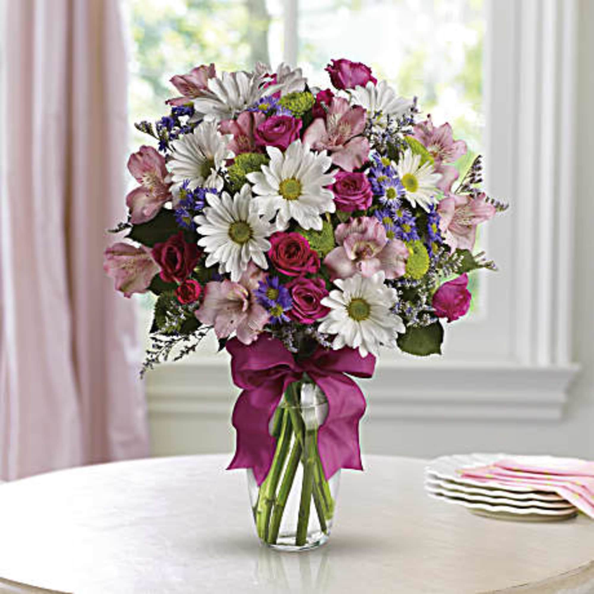 Mixed bouquet of pink and white flowers in a clear glass vase with a magenta ribbon