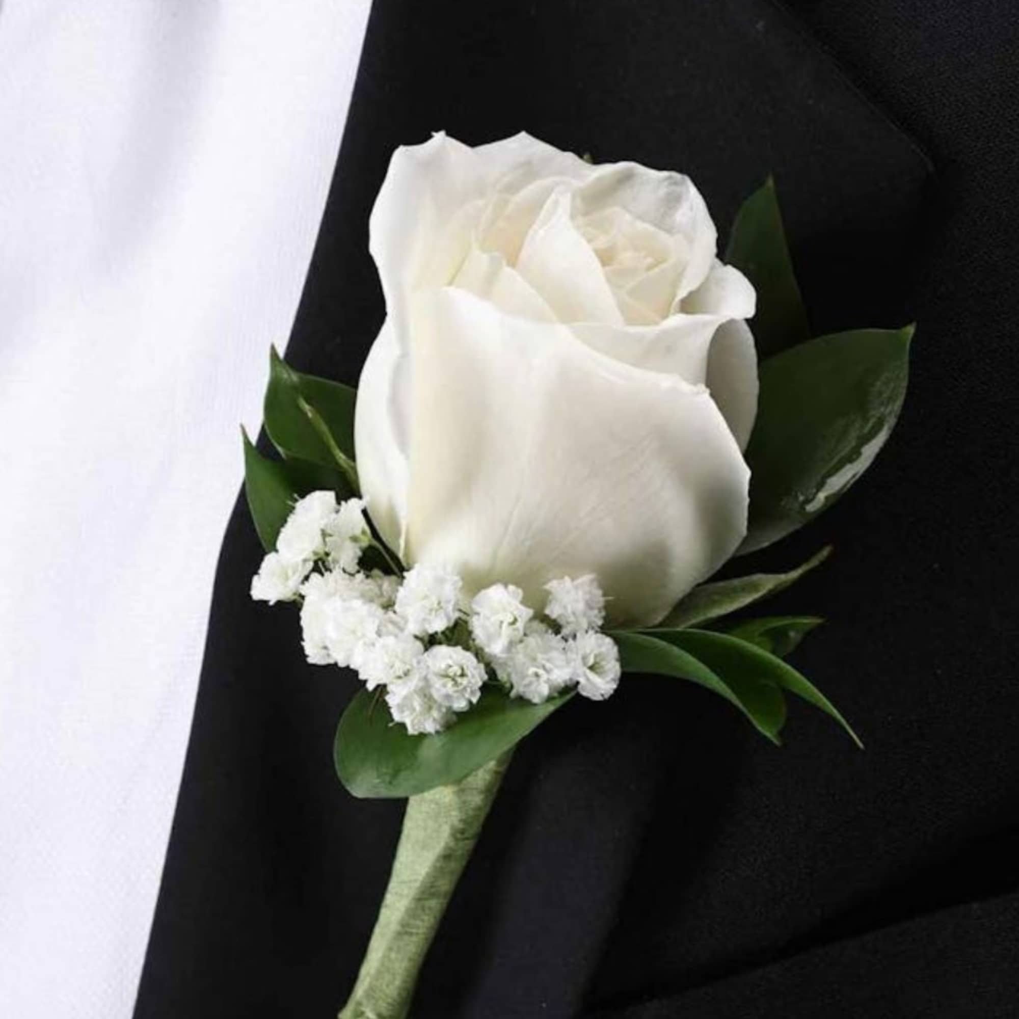 White rose boutonniere with small white filler flowers on black fabric