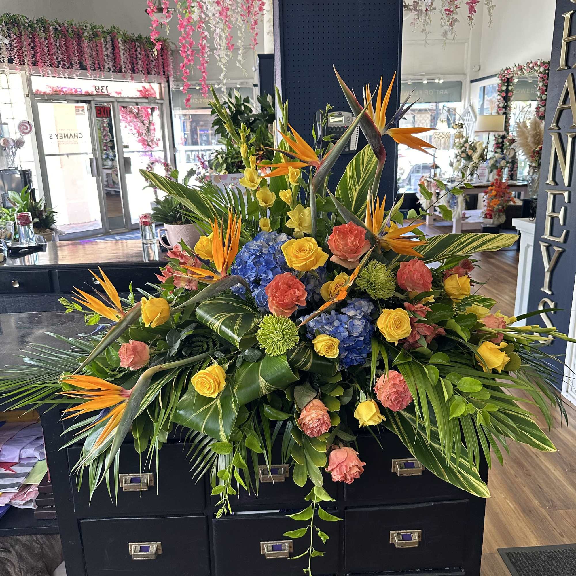 Large tropical floral arrangement with birds of paradise, roses, hydrangeas, and greenery