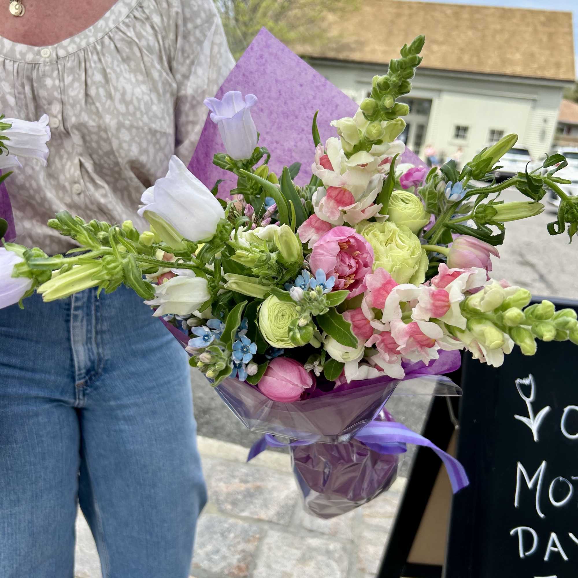 Handheld bouquet of pink, white, and green flowers wrapped in purple paper