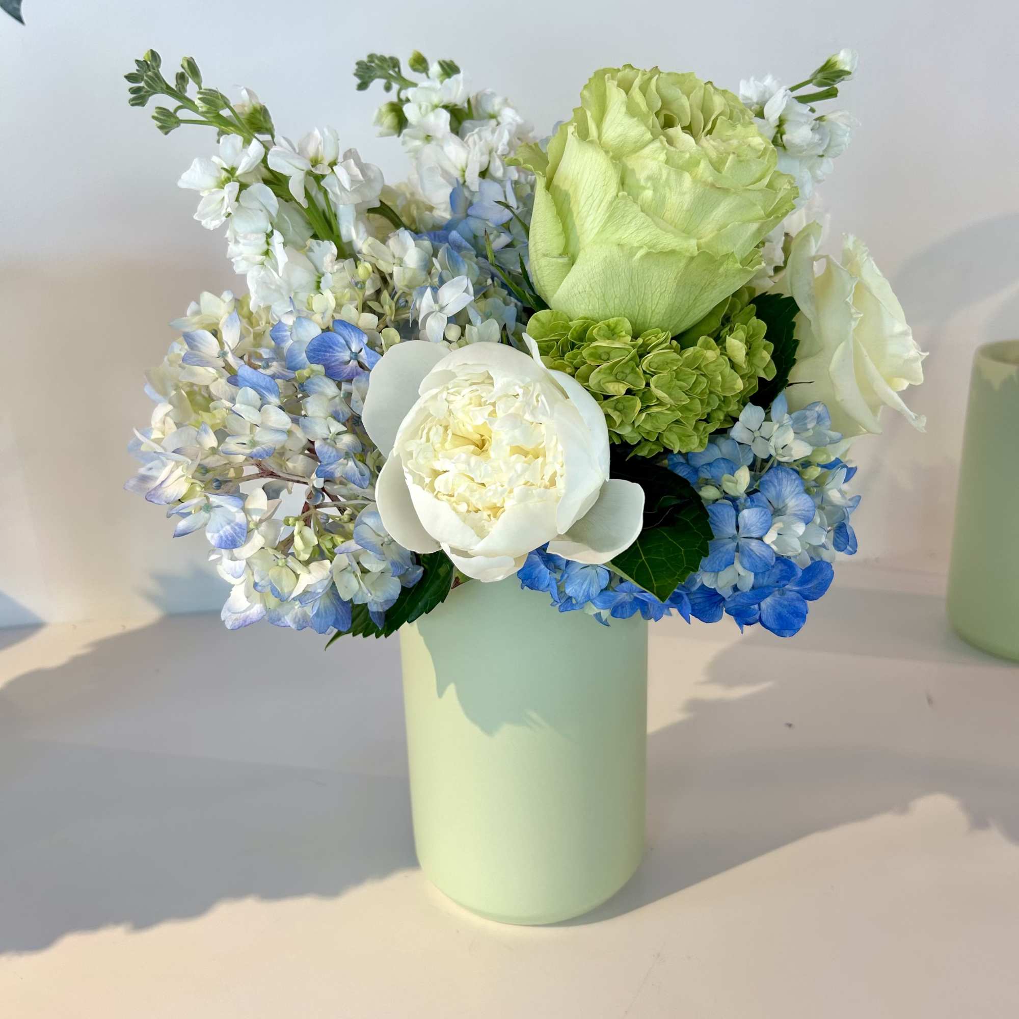 Blue and white flowers with green roses in a pale green vase