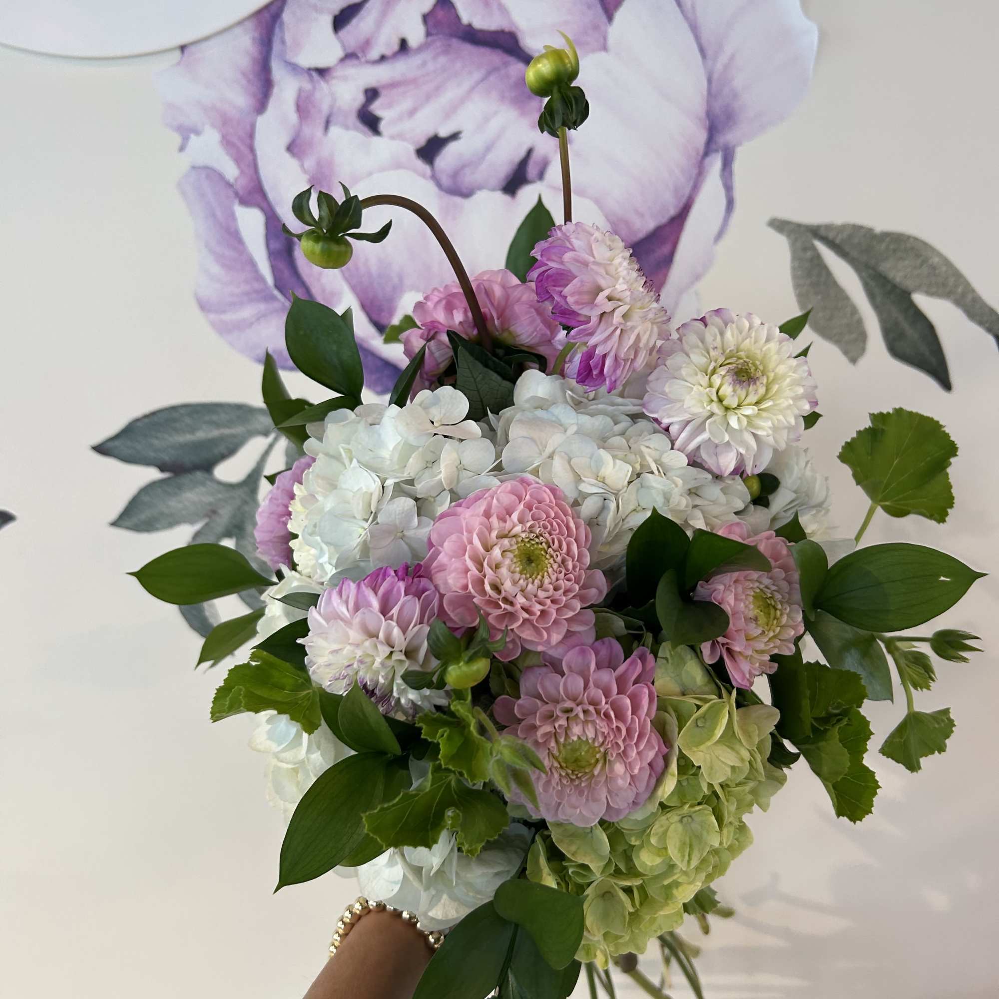 Handheld bouquet of pink, white, and green flowers with leafy accents