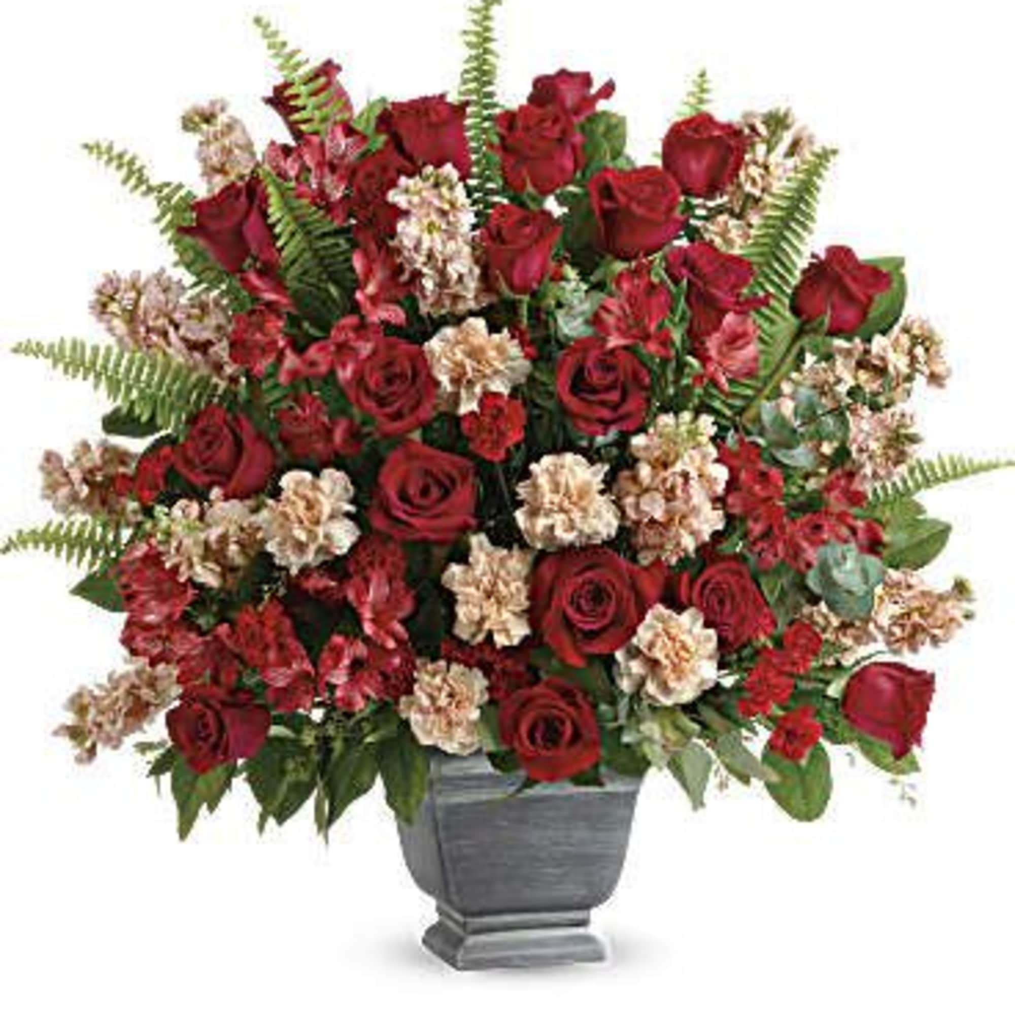 Red roses and pale filler flowers in a gray urn vase