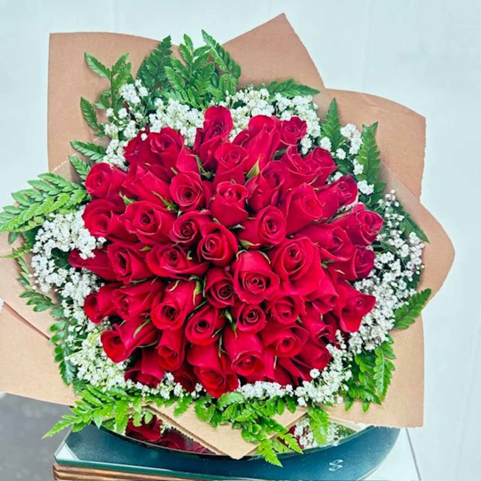 A dense, hand-tied cluster of vivid red roses-framed by delicate white filler