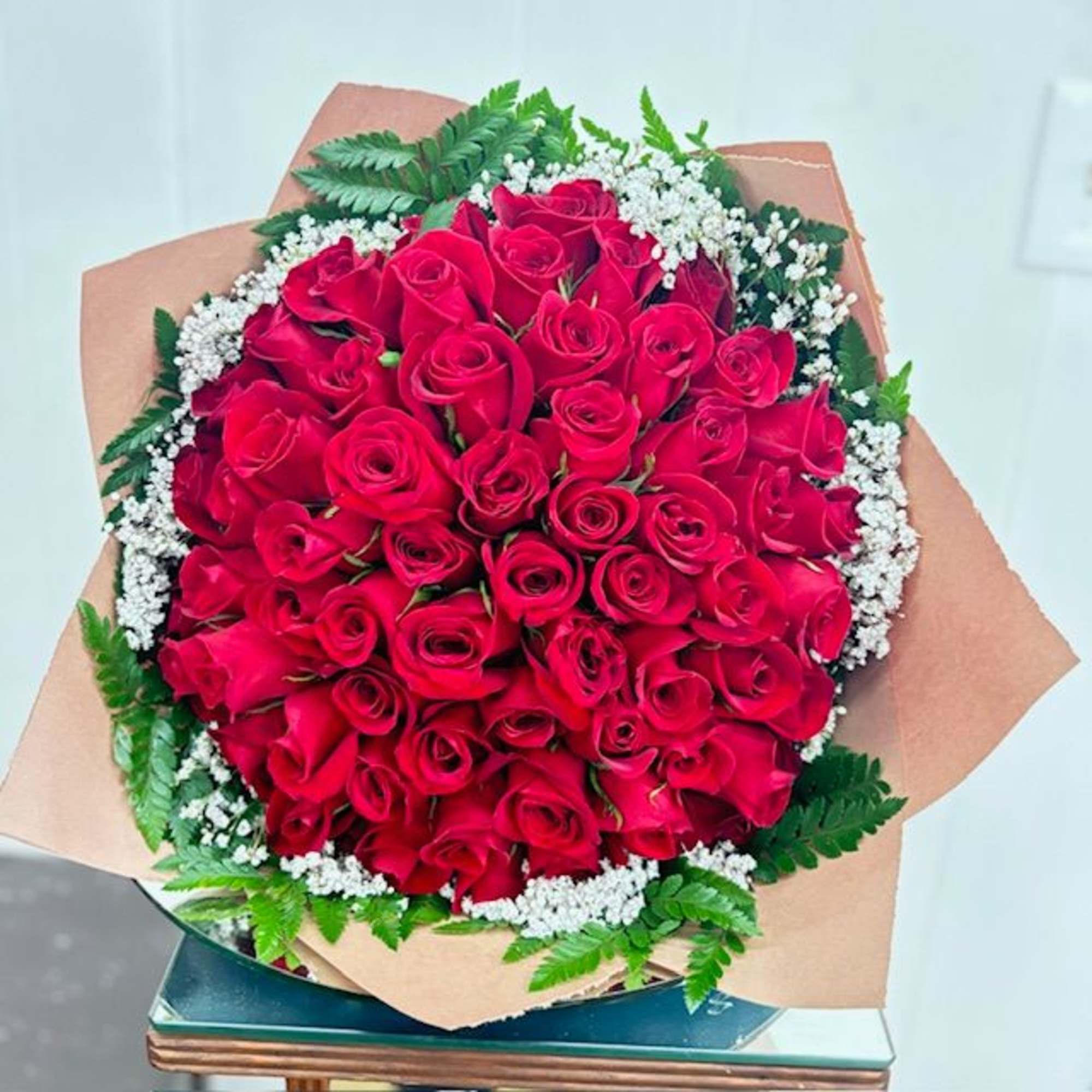 A dense, hand-tied cluster of vivid red roses-framed by delicate white filler