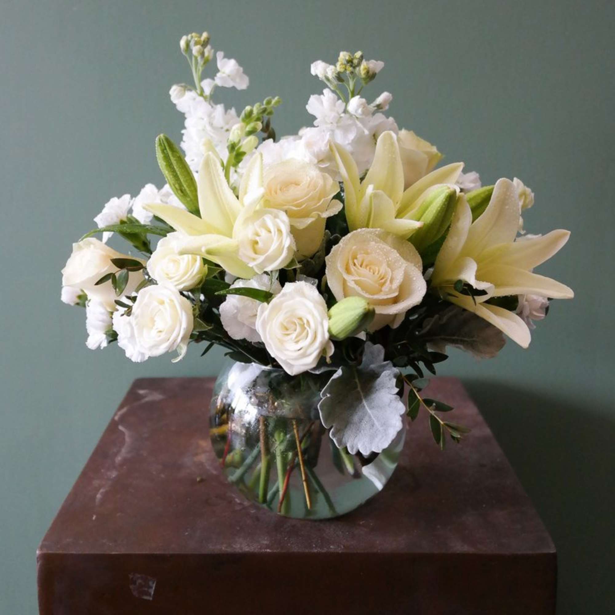 White lilies and roses arranged in a round glass vase